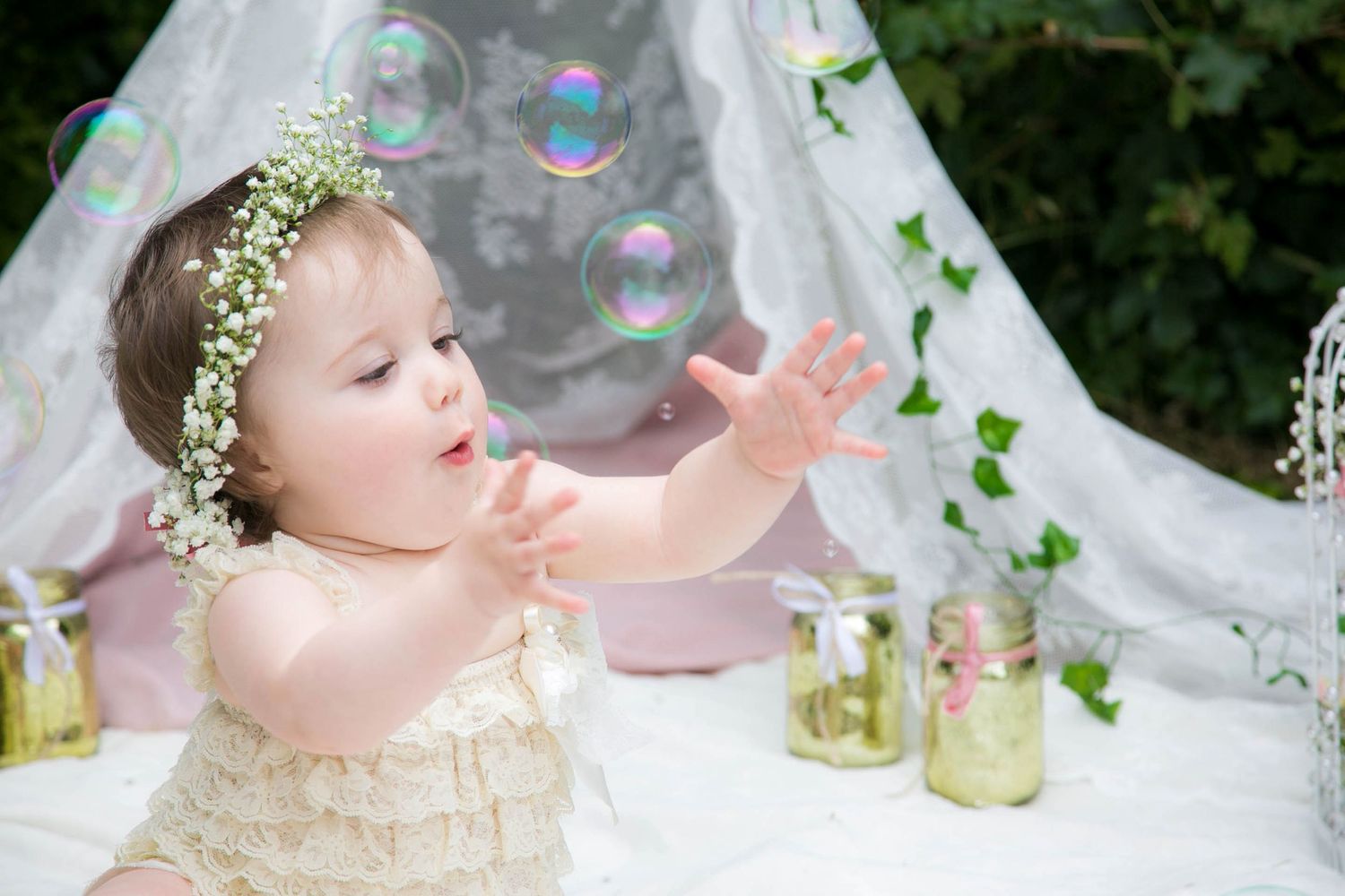 outdoor cake smash photo shoot, baby catching bubbles, dressed in boho wearing a flower crown
