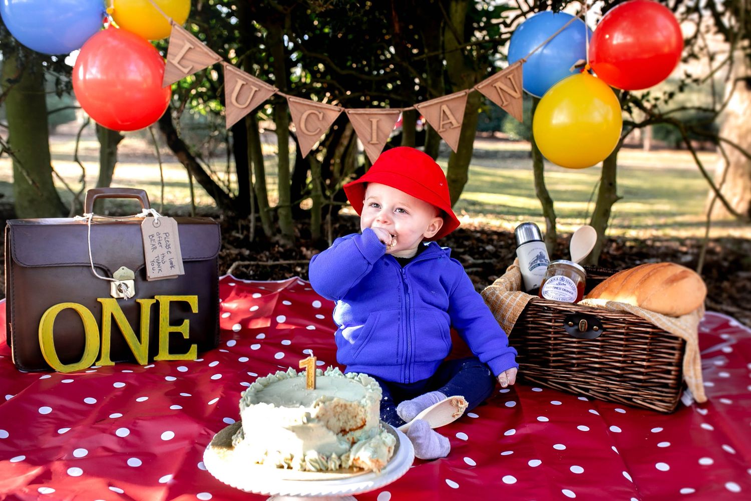 One year old boy dressed at paddington bear with balloons and props around him for his cake smash photo shoot