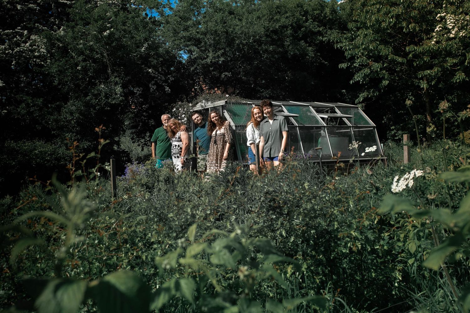Three pairs of couples outside their family green house in their allotment