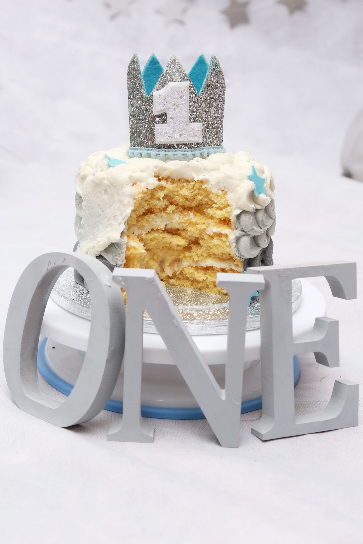 Detail photo of a 1 year olds cake smash smash with ONE letters in front. Cake is open showing the victoria sponge inside