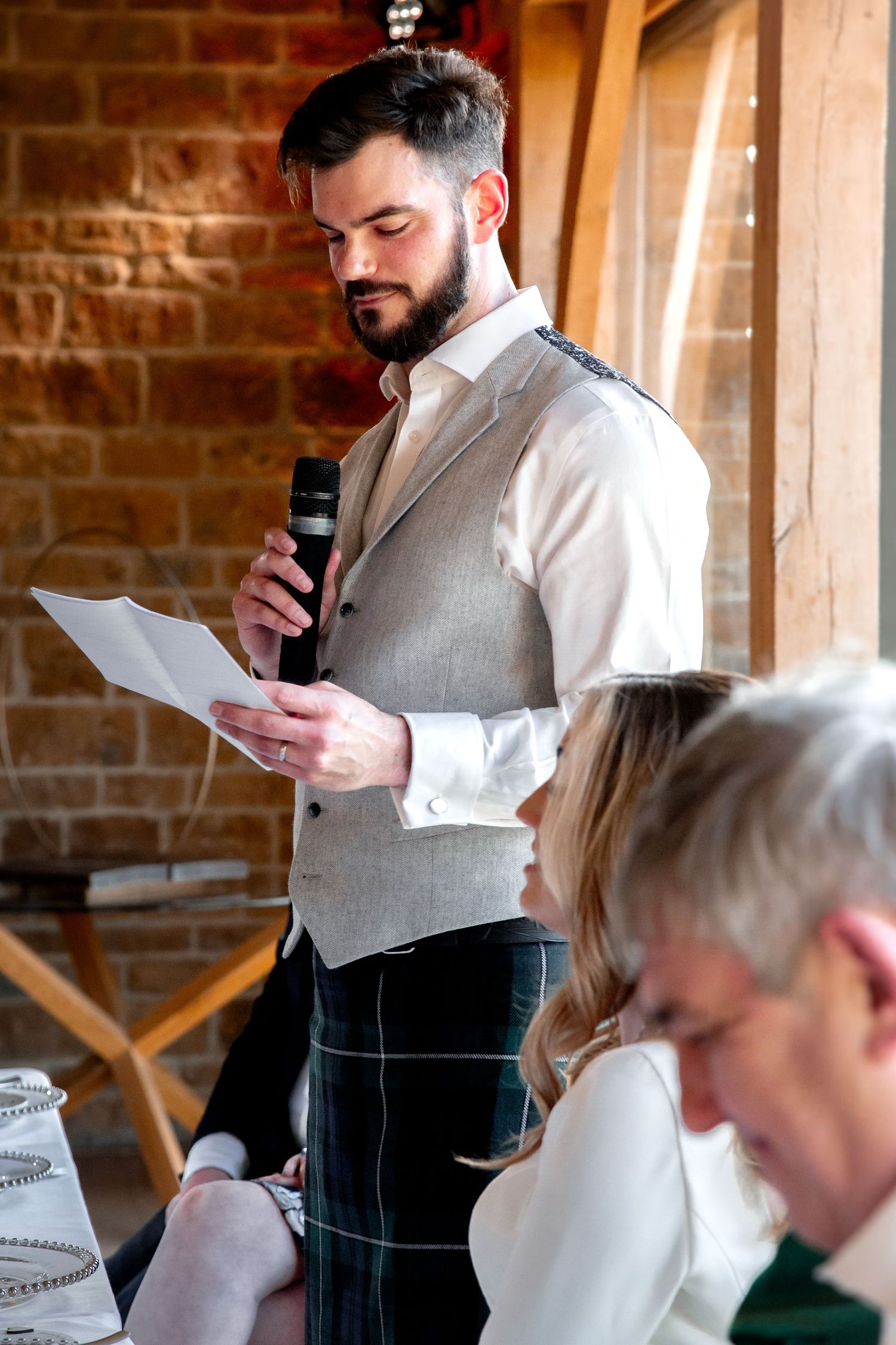 Groom at Dodford Manor standing up with paper and a microphone, talking to guests, doing his speech