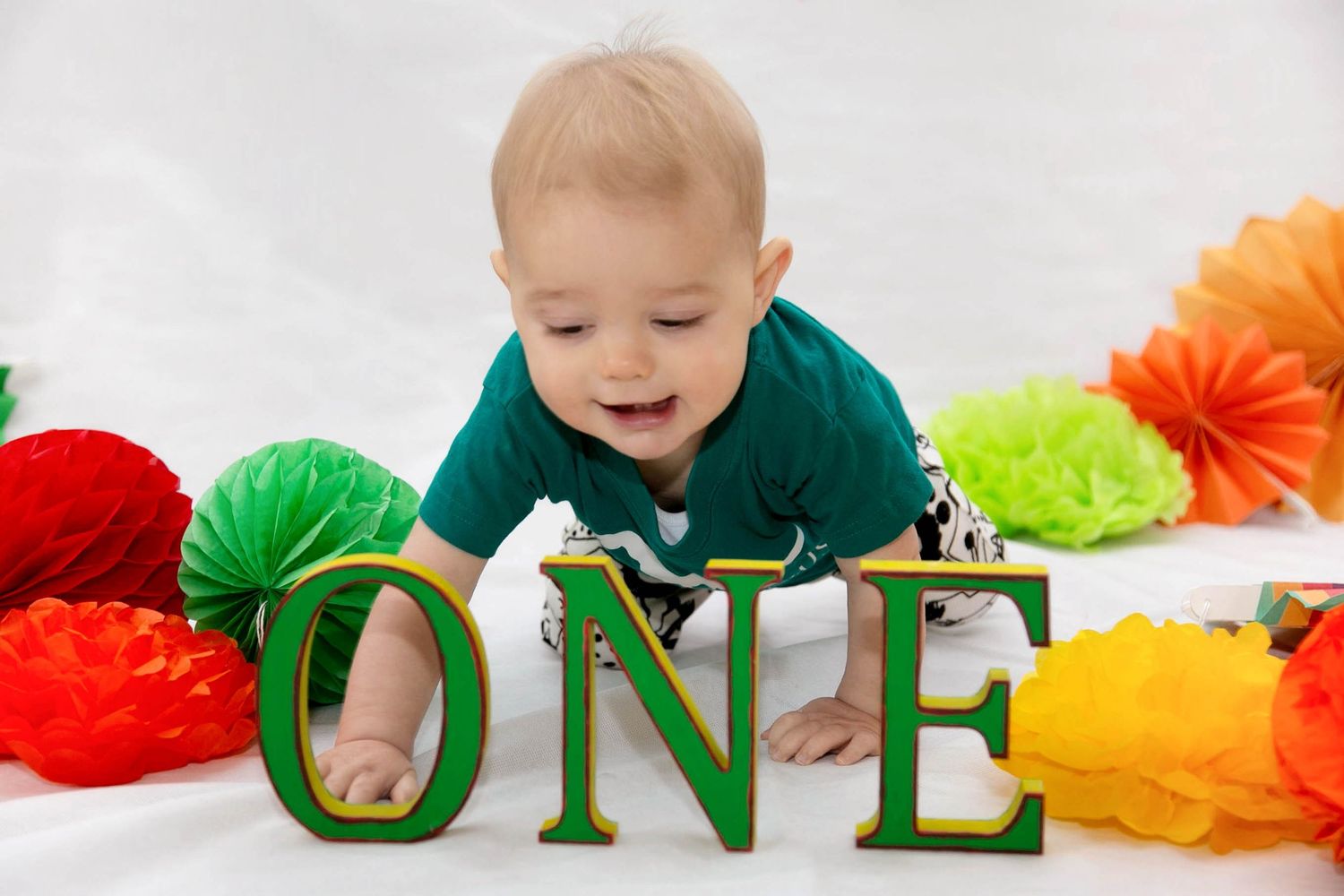 baby boy during his first birthday photo shoot, with brightly coloured props including the green O N E letters in front
