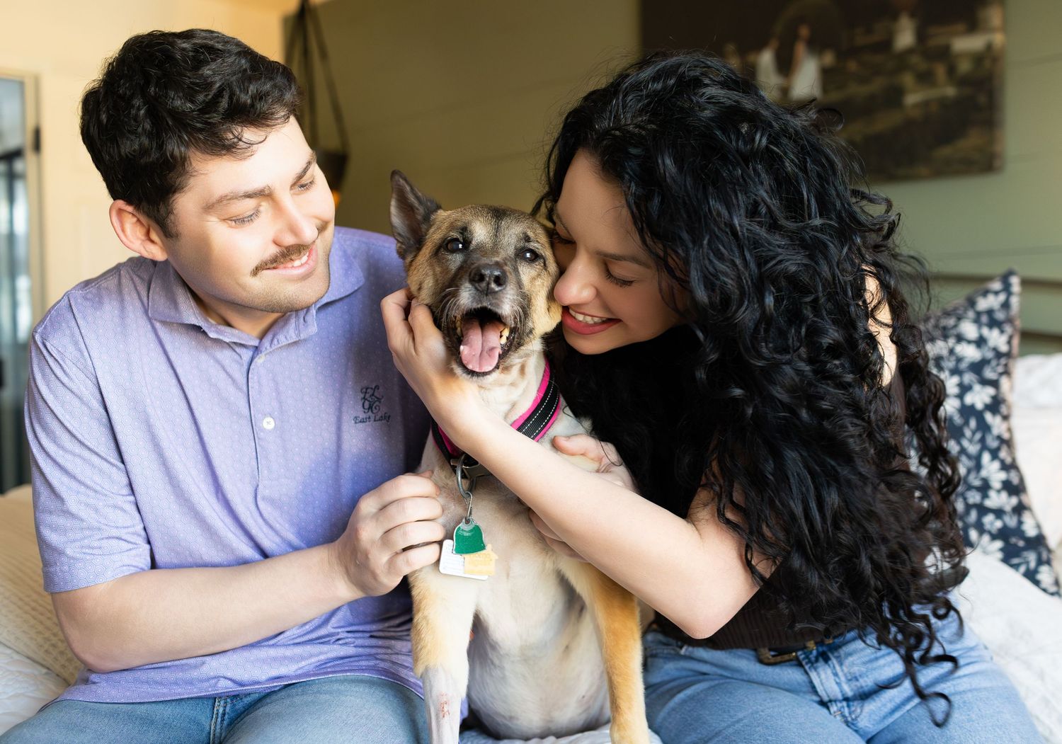A couple smiles while petting their happy German Shepherd mix dog indoors.