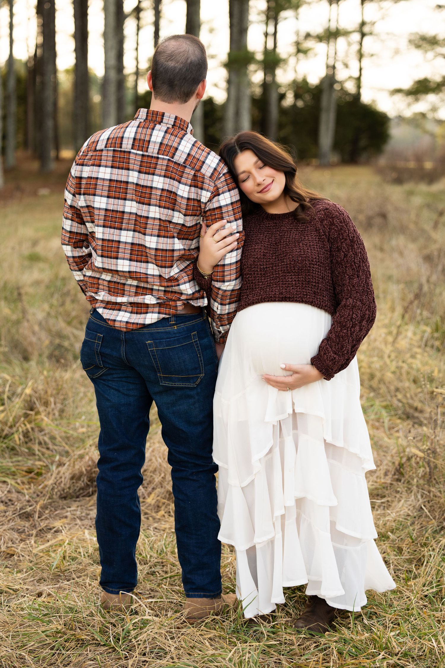 A couple in casual attire embraces tenderly in a sunlit forest setting during an outdoor photo session.