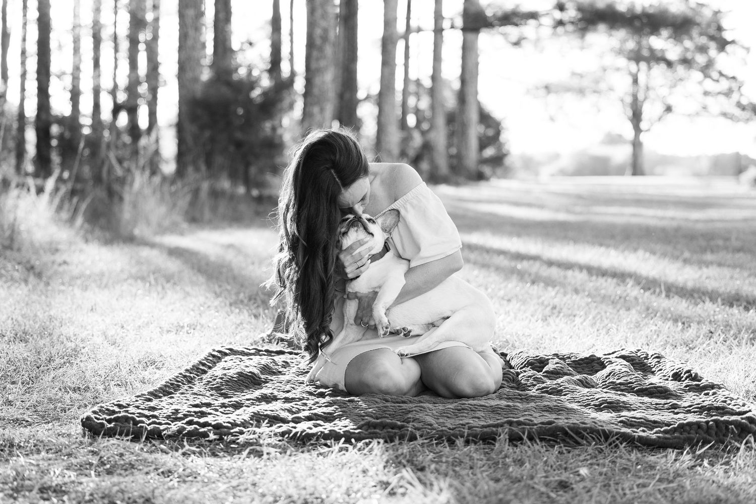 A person sits on a blanket in a wooded area, captured in black and white photography.