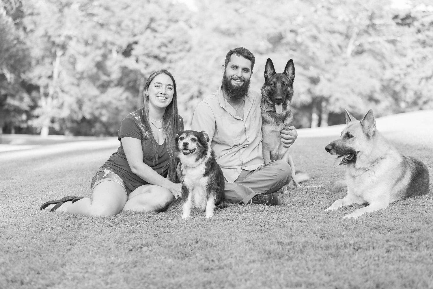 A couple lays on grass outdoors spending time with their pet Corgi dog in a relaxed summer setting.