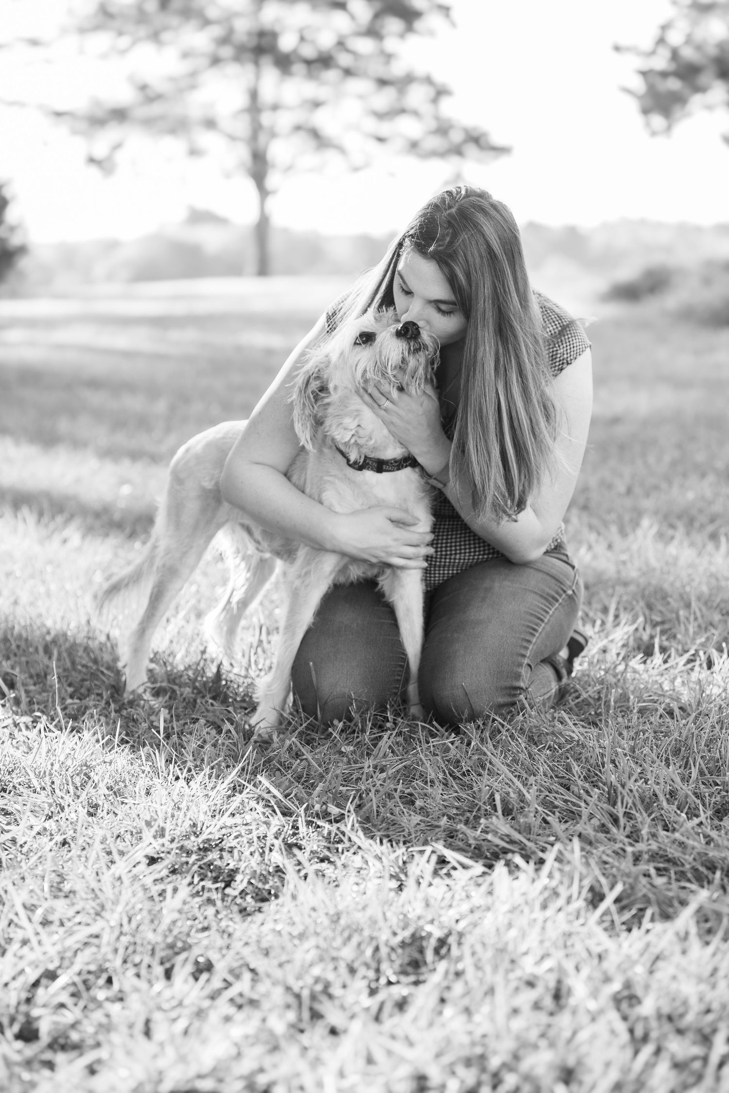 A tender moment captured in black and white as someone embraces their loyal dog in a sunlit field.