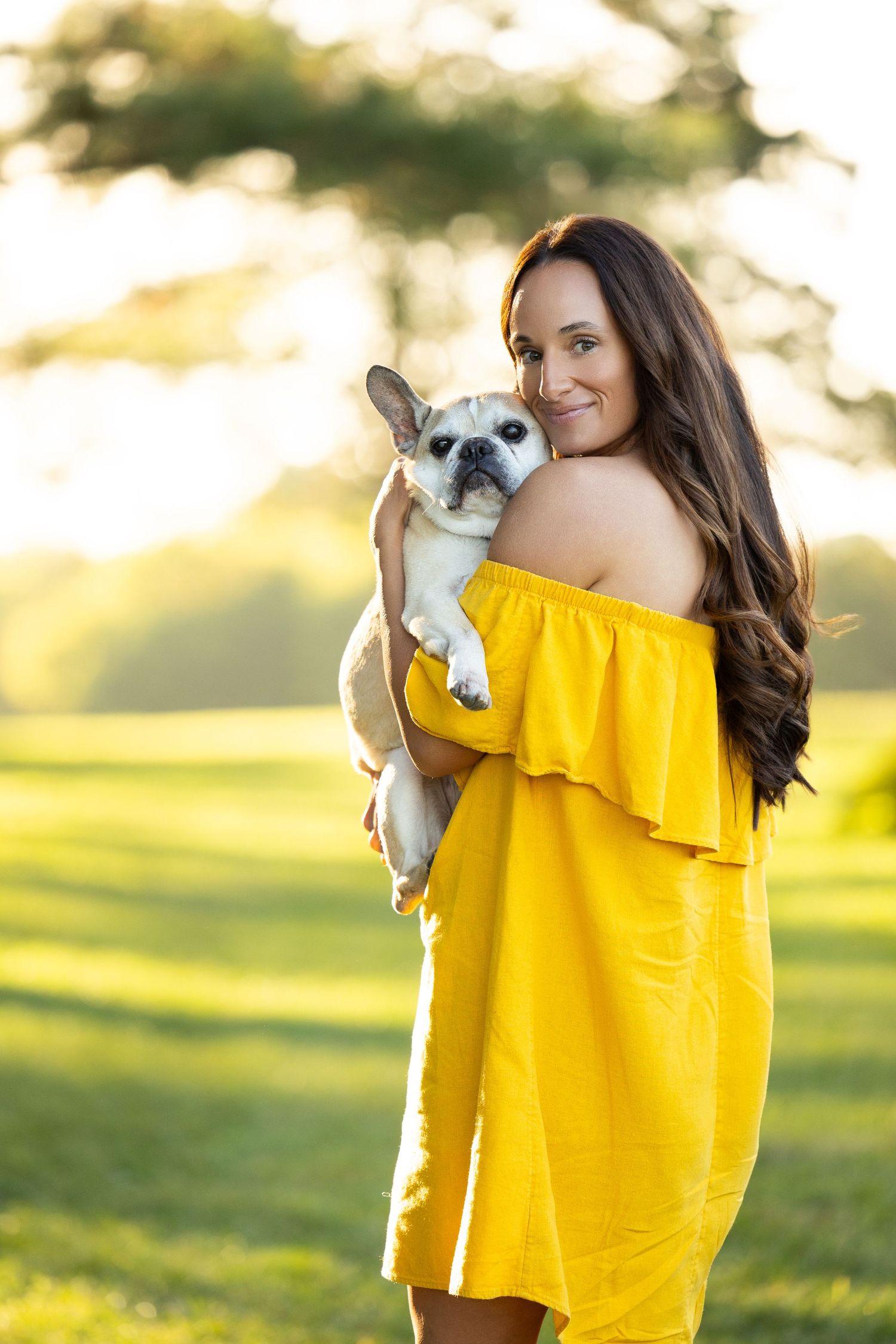 Woman in bright yellow off-shoulder top holds small white Chihuahua dog in sunny outdoor setting.