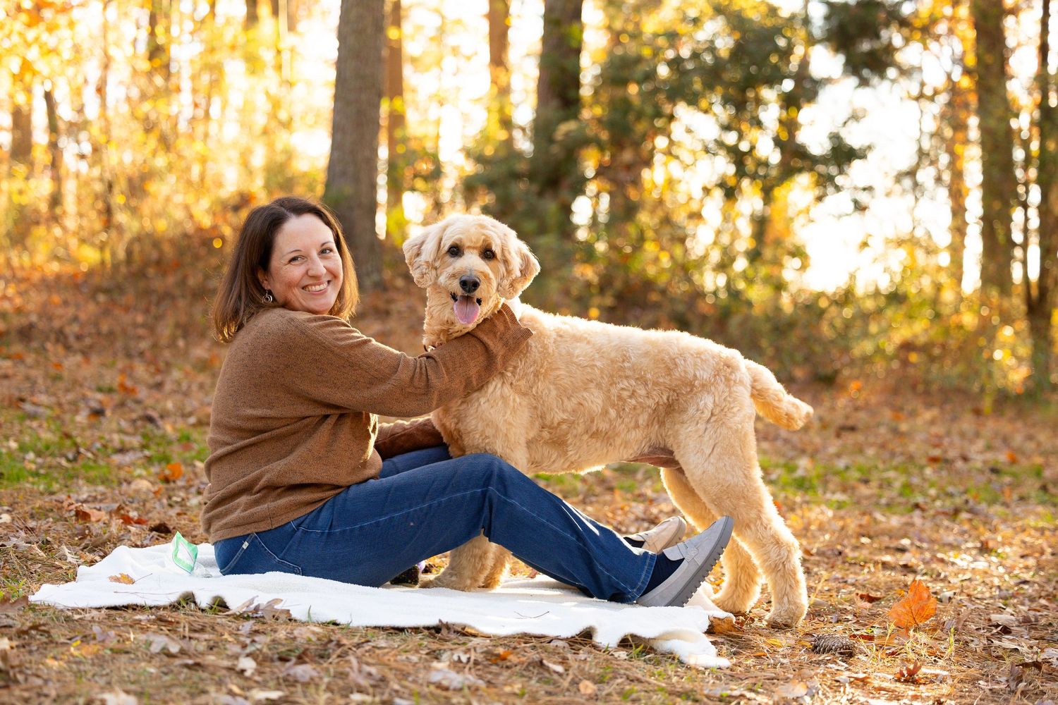A person and golden retriever dog relaxing on a blanket in a sunlit autumn forest during golden hour.