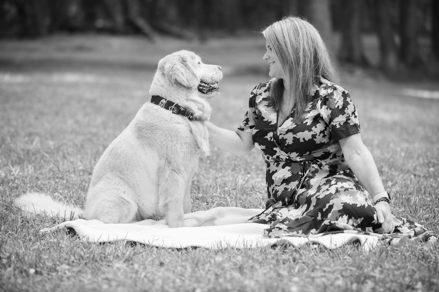Heartwarming black and white photo showing a person sitting on blanket and interacting joyfully with a Golden Retriever.
