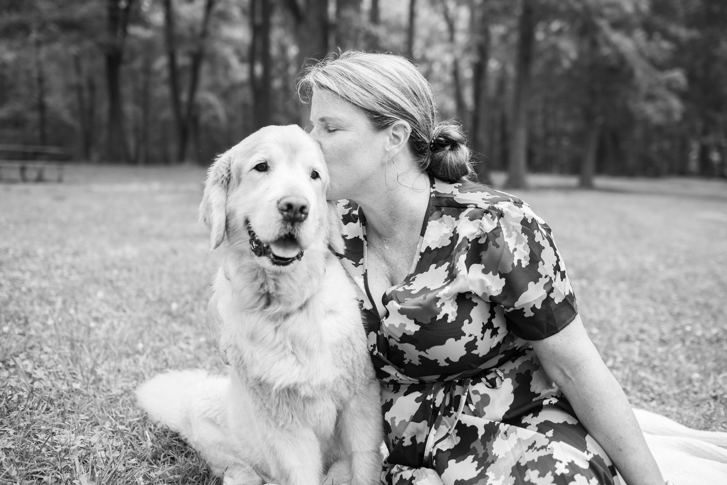 Sweet candid moment between person in floral dress and their Golden Retriever dog sitting together in a park.