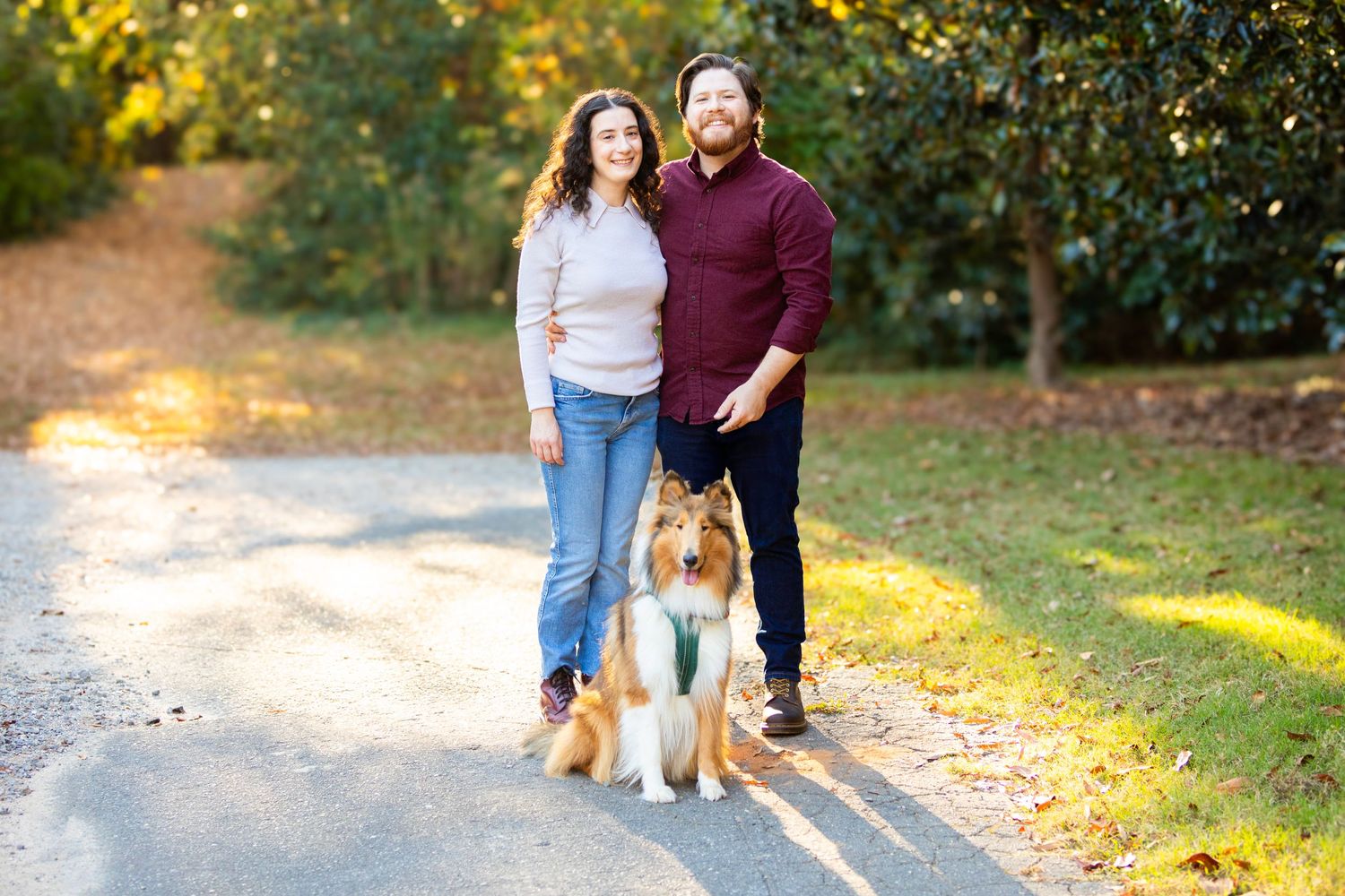 Dog with two people on a tree-lined path during golden hour.