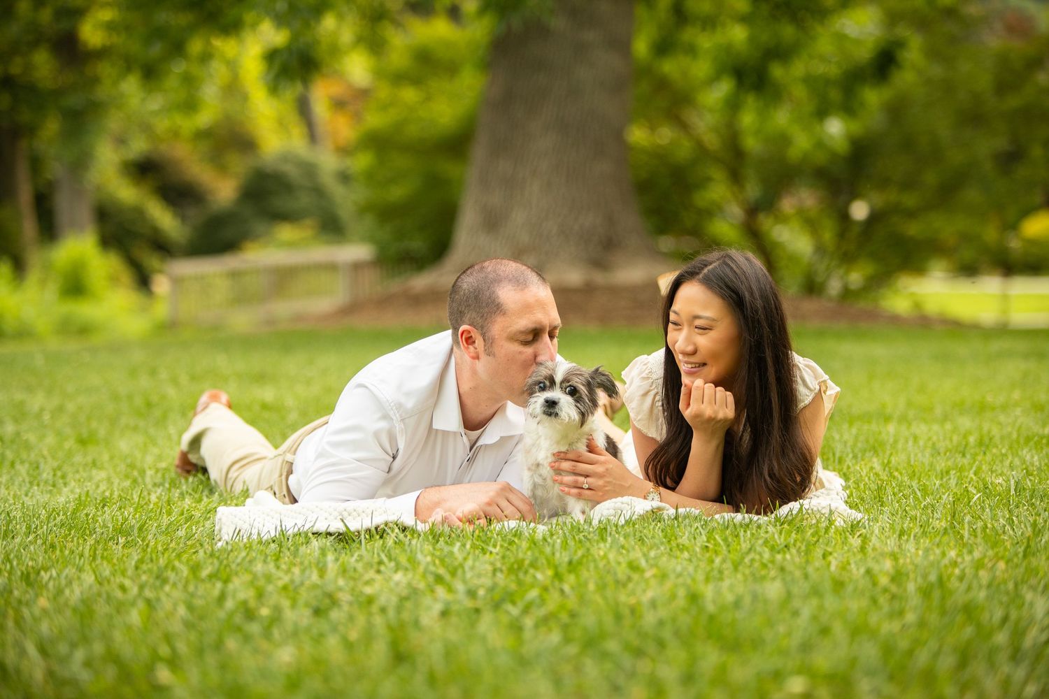 Two figures lying on green grass in a park setting while reading books on a sunny summer day.