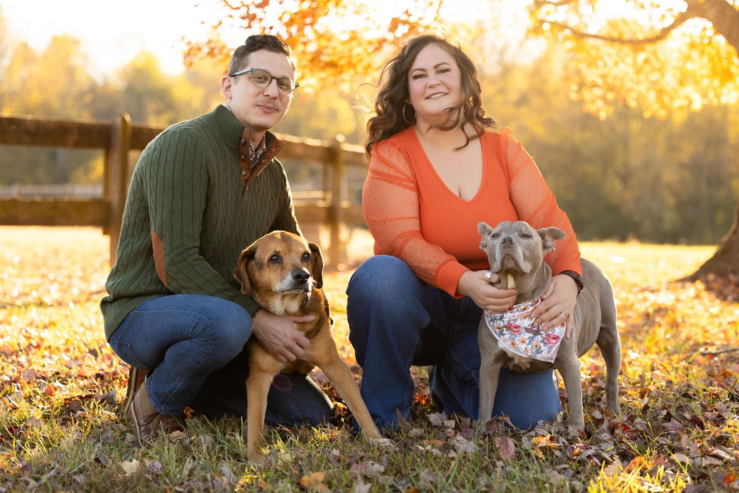 A couple sits with their dog in autumn leaves during a golden sunset photo session.