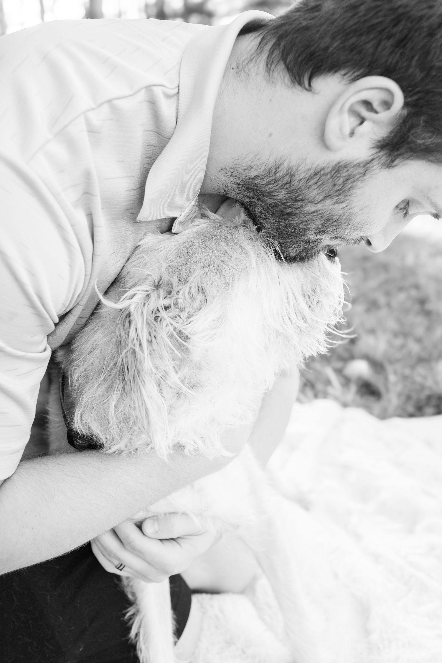 A black and white close-up photo of someone sharing a tender moment with a white, fluffy dog.