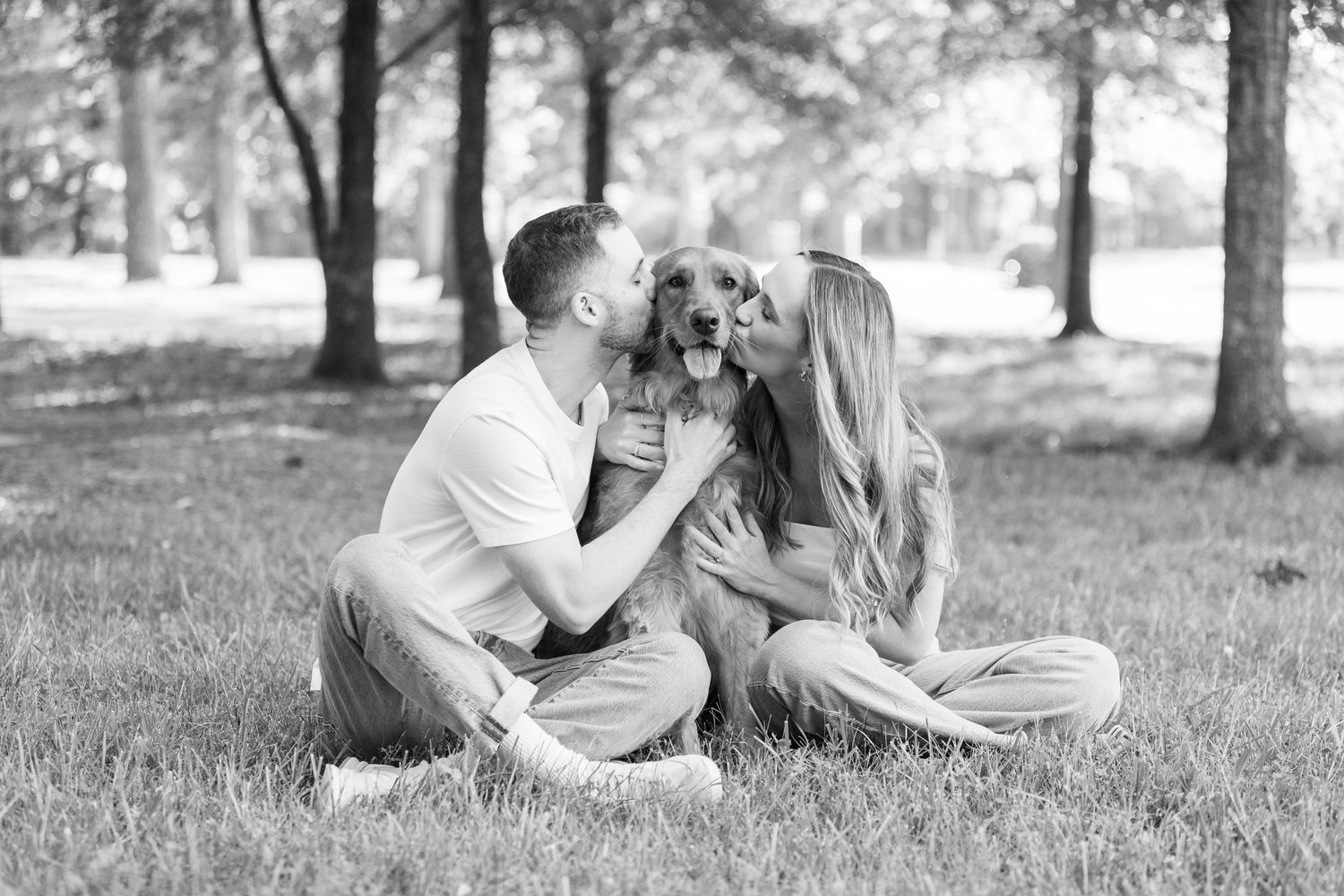 A romantic couple shares tender moments together while sitting on grass in a park setting, shown in black and white.