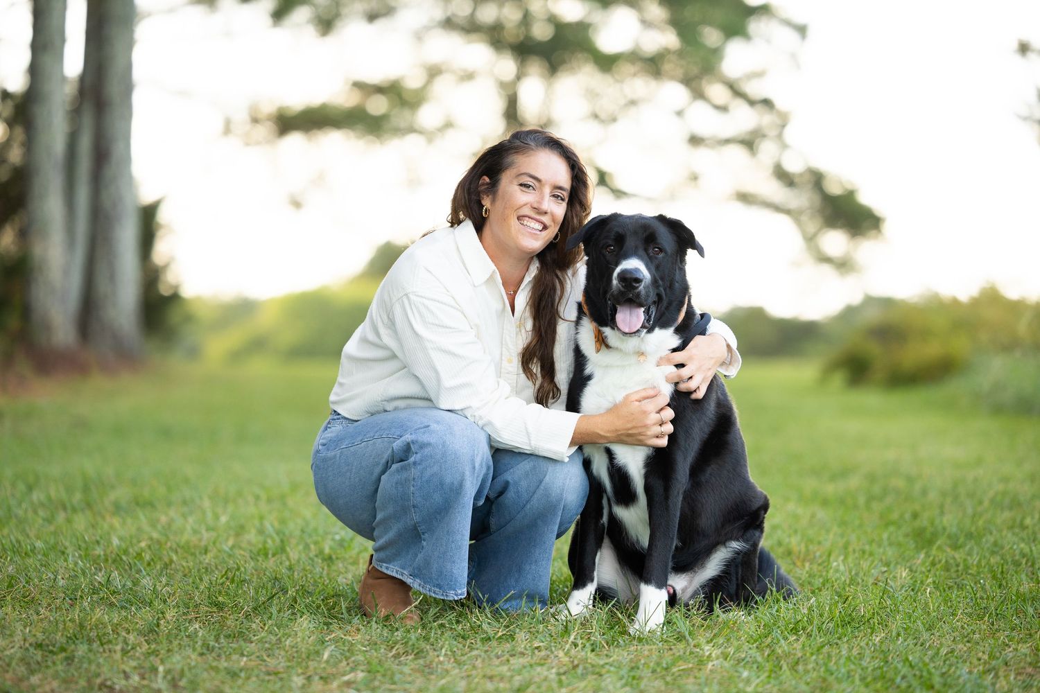 A black and white border collie dog plays and poses with someone on green grass in a park setting.