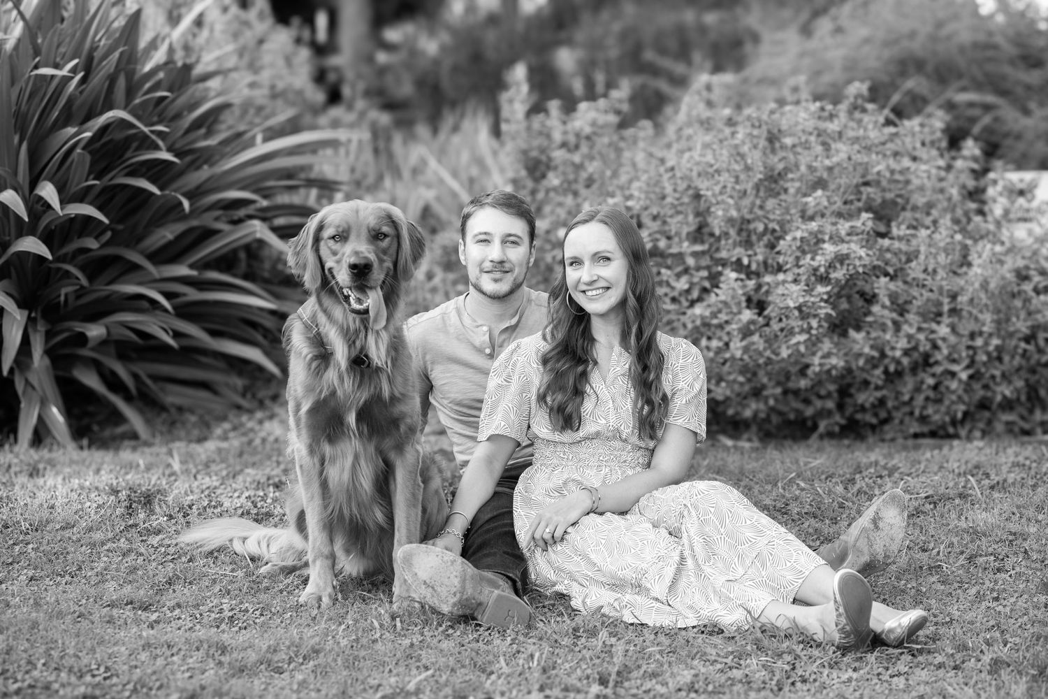 Dog and loved ones resting together outdoors on green grass in black and white photography series.