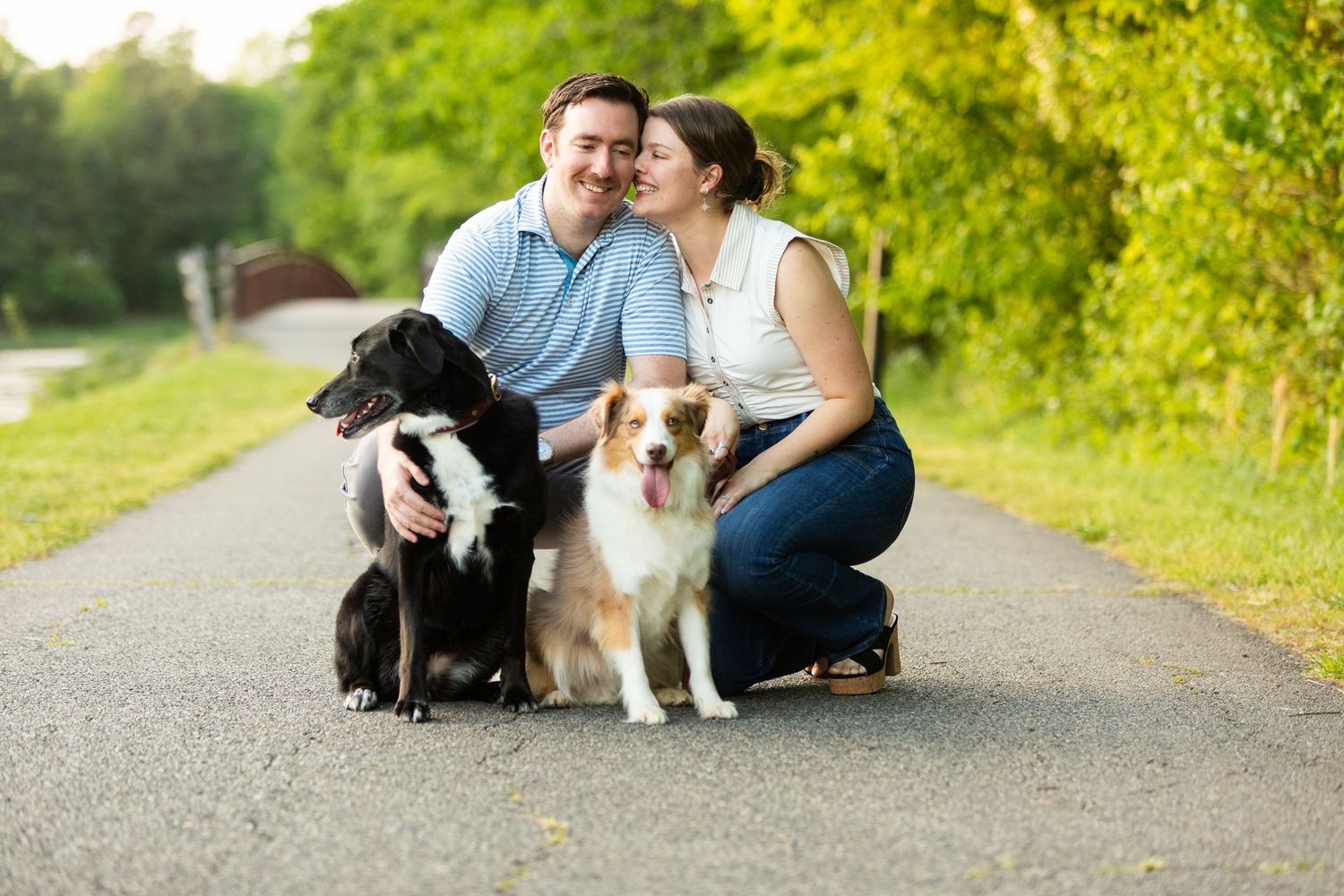 Two dogs and their owners sharing a joyful moment together on a sunny path surrounded by lush greenery.