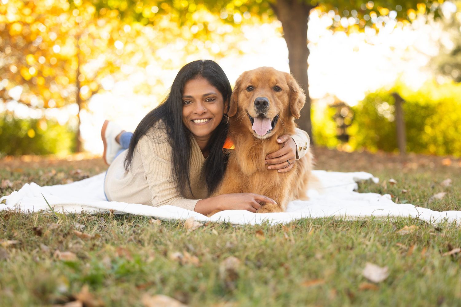 A person and golden retriever dog lying together on grass during a sunny autumn day.