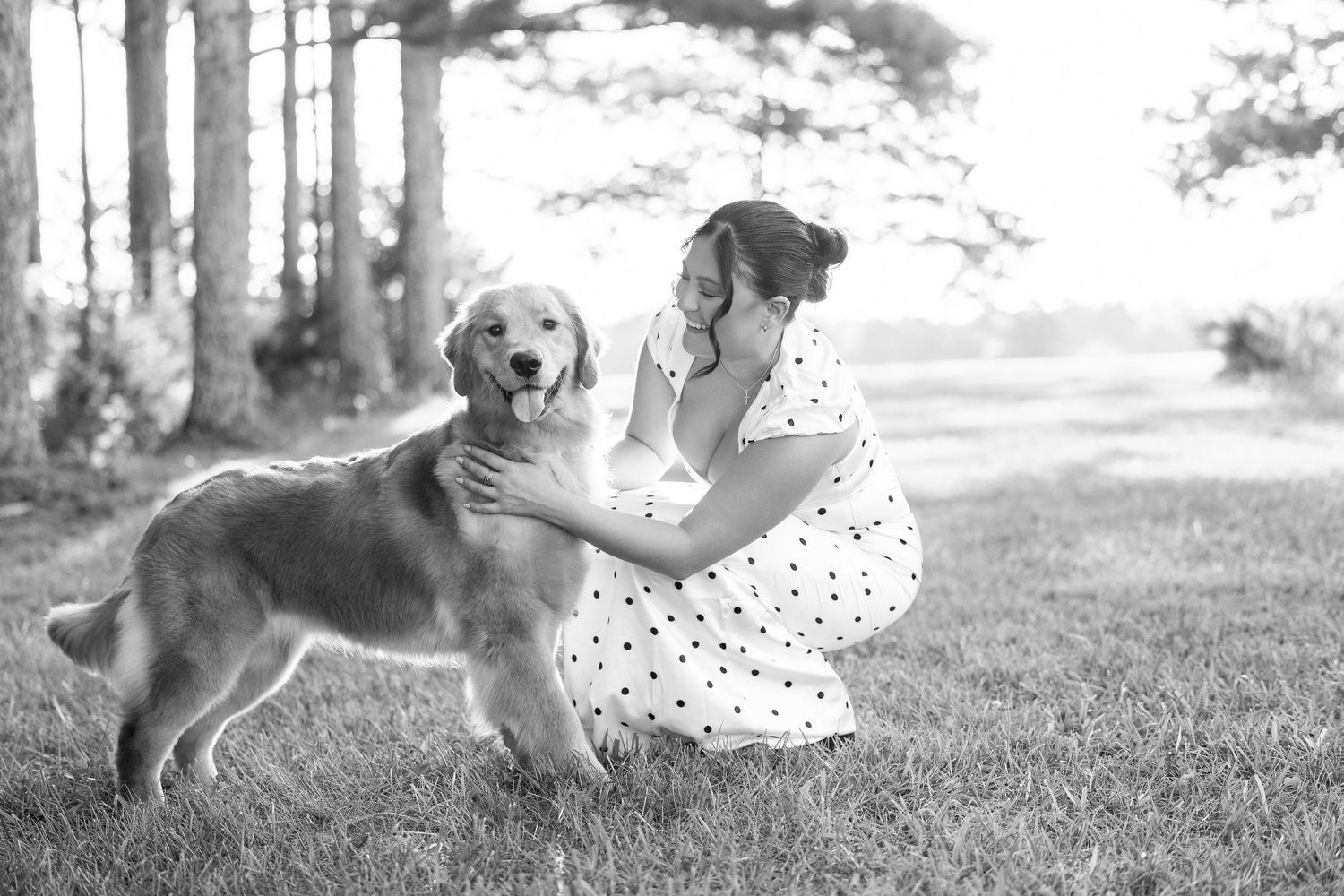 Black and white photo of a woman in a polka dot dress affectionately petting a golden retriever on a grassy lawn.