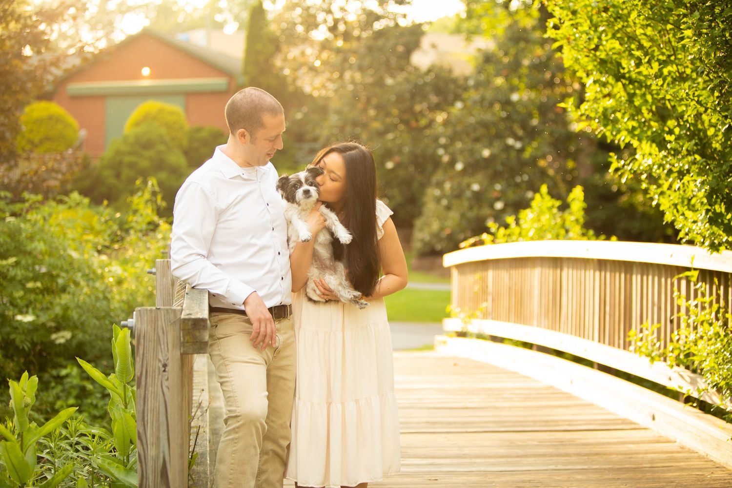 A couple laughs together while standing on a wooden boardwalk surrounded by lush greenery.