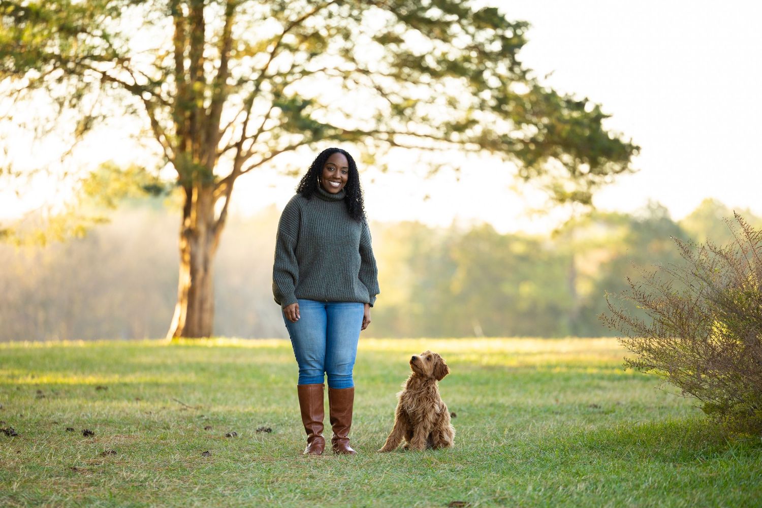A person and a brown dog walk together on a grassy path during golden hour sunset.