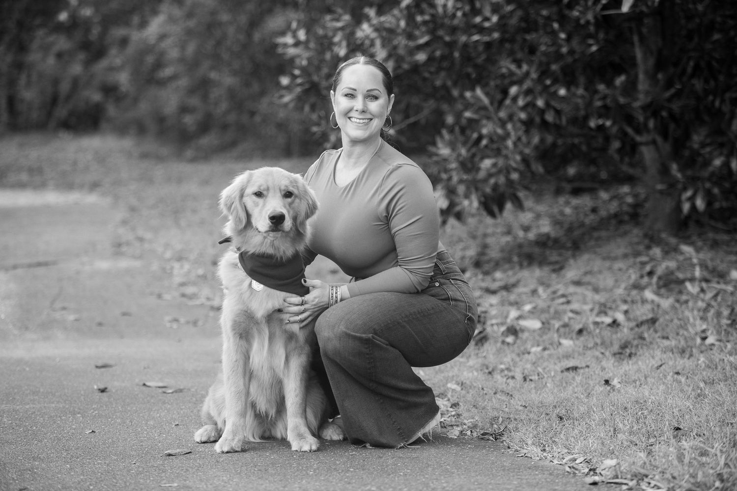 A Golden Retriever and companion pause together on a nature path in a black and white photograph.