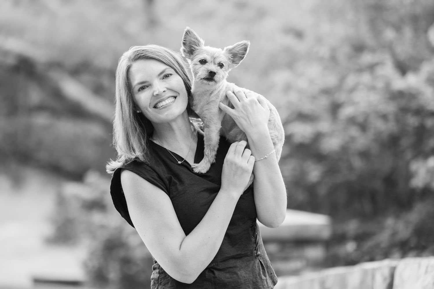 Black and white photo of someone holding a small Chihuahua mix dog outdoors.
