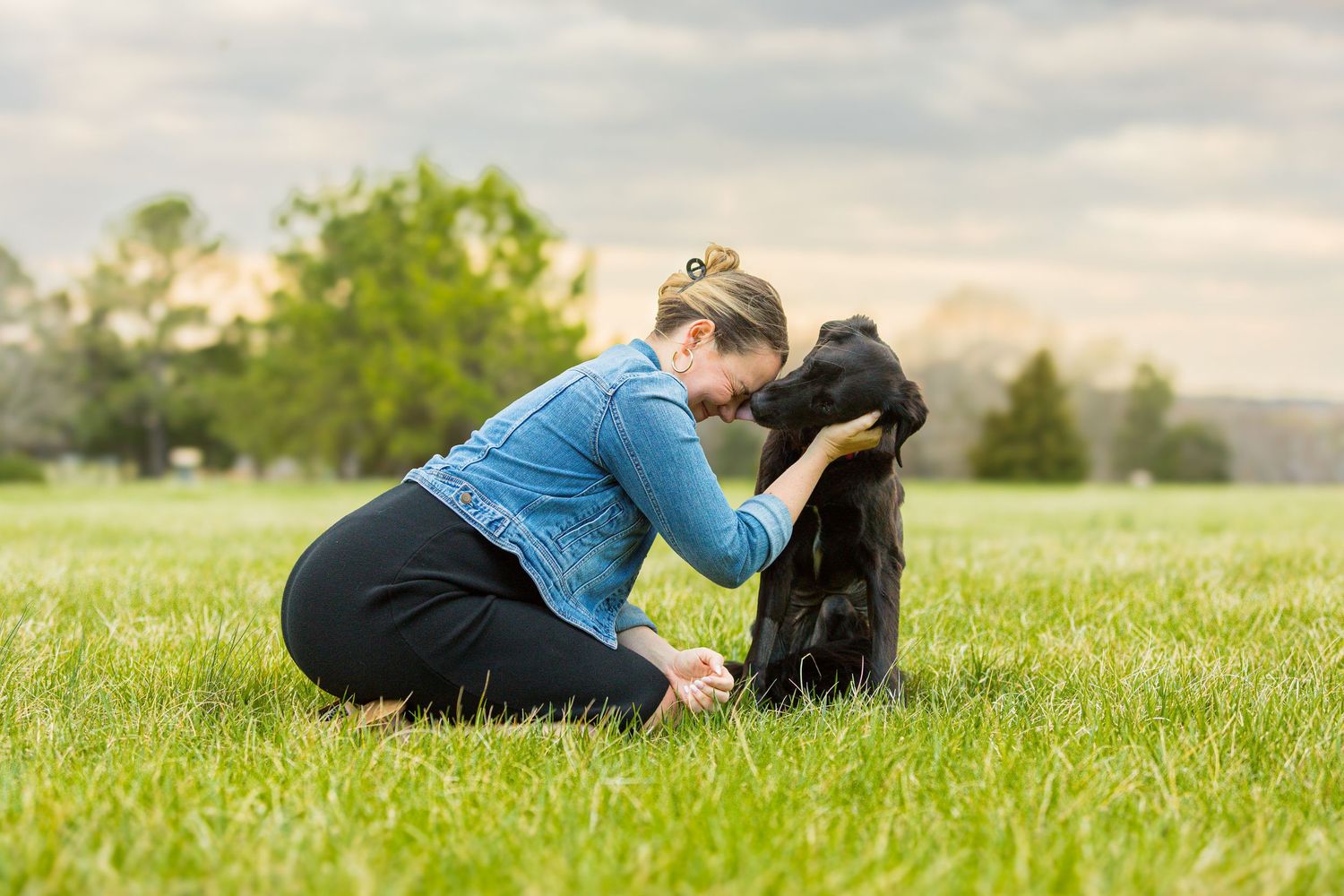 Someone lying in green grass next to a black dog on a sunny spring day, reading and relaxing together.