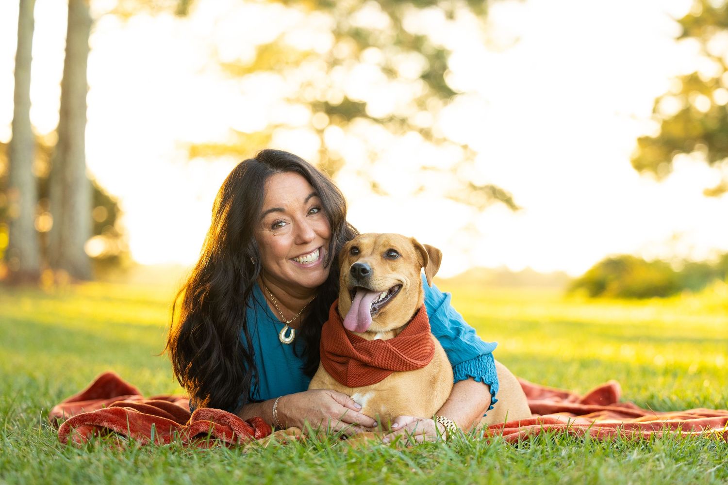A person and their dog share a tender moment on a red blanket in a sunlit park during golden hour.