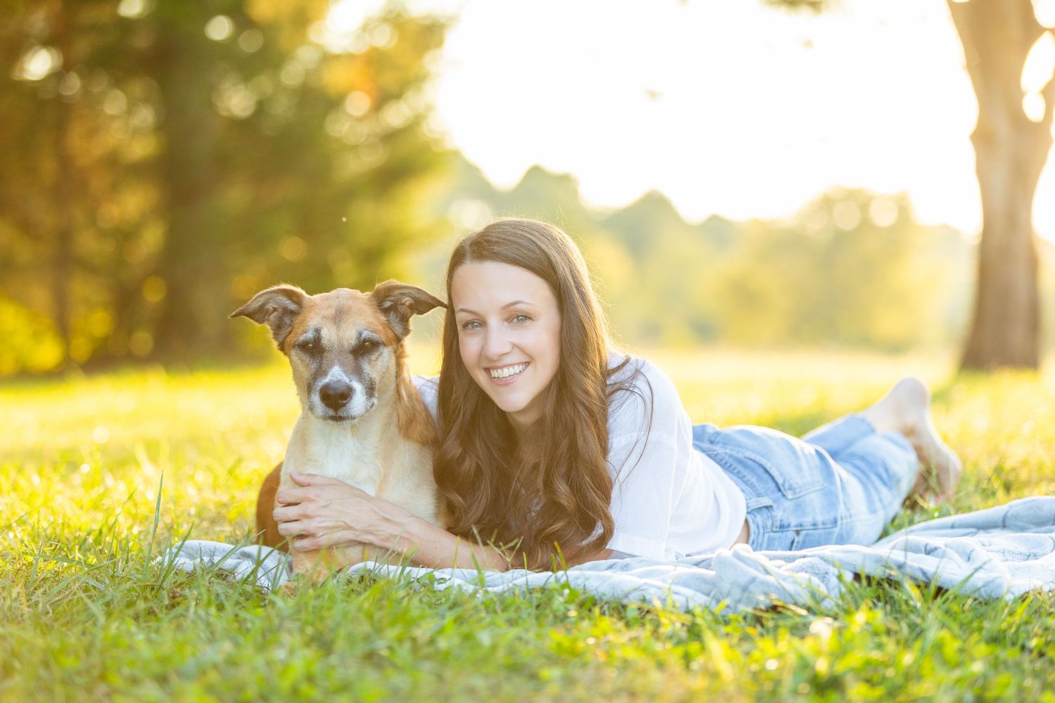 A person lies on grass at sunset with their dog while reading a book in a peaceful outdoor setting.