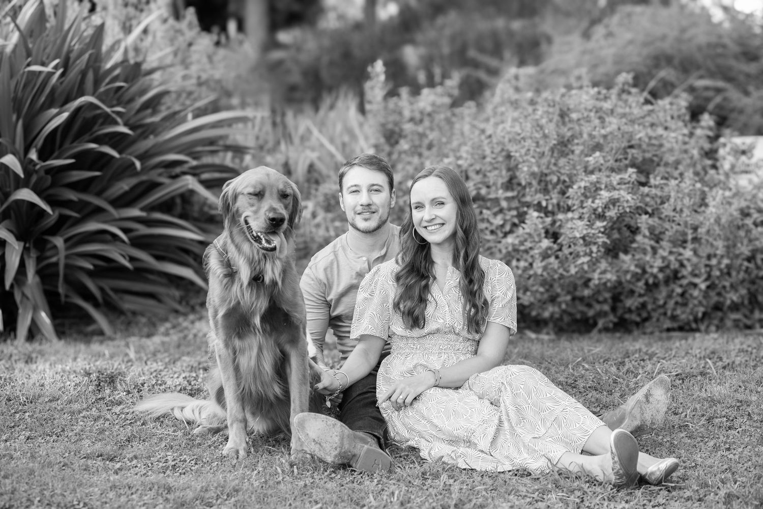 Black and white photo of people sitting in a garden with their golden retriever dog.