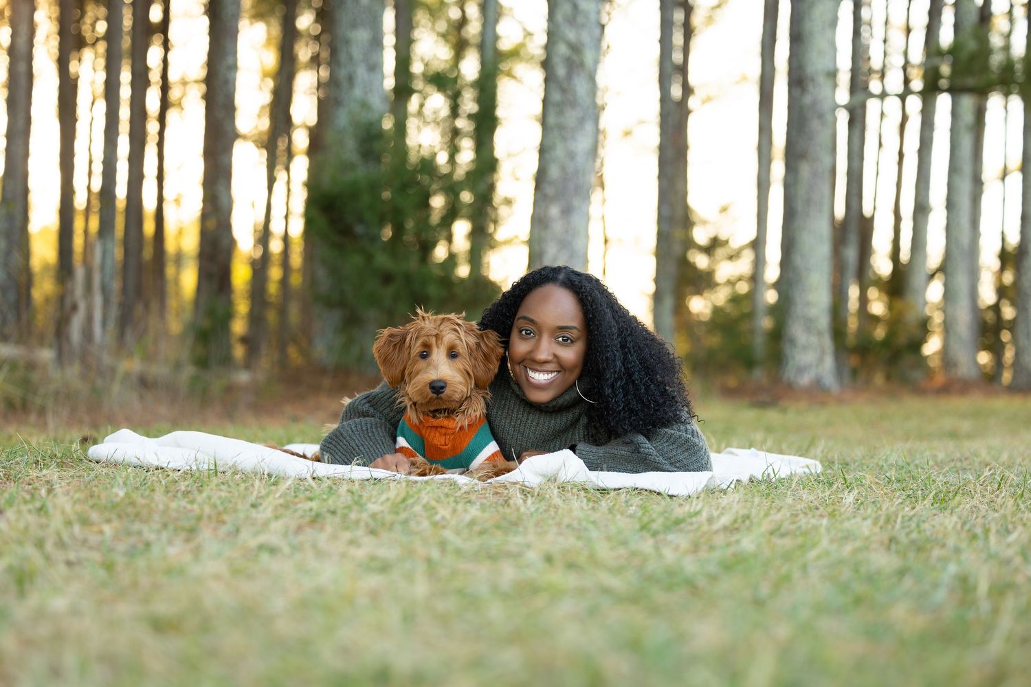 People lying on autumn grass in a wooded area during a fall photoshoot at sunset.