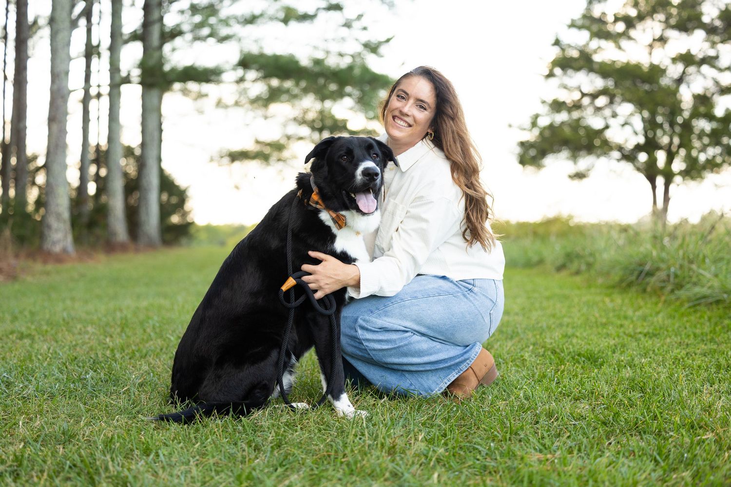 A person plays and interacts with a black labrador retriever dog in a grassy outdoor setting.