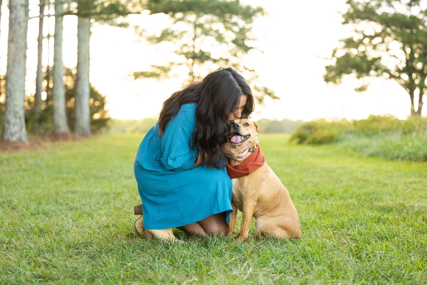Person and golden retriever sharing an affectionate moment outdoors on grass with trees in background.