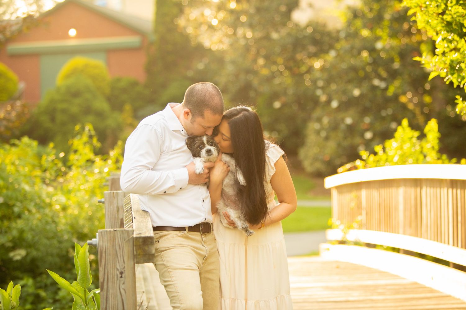 A romantic couple embraces on a wooden deck during golden hour sunset with warm glowing light filtering through trees.
