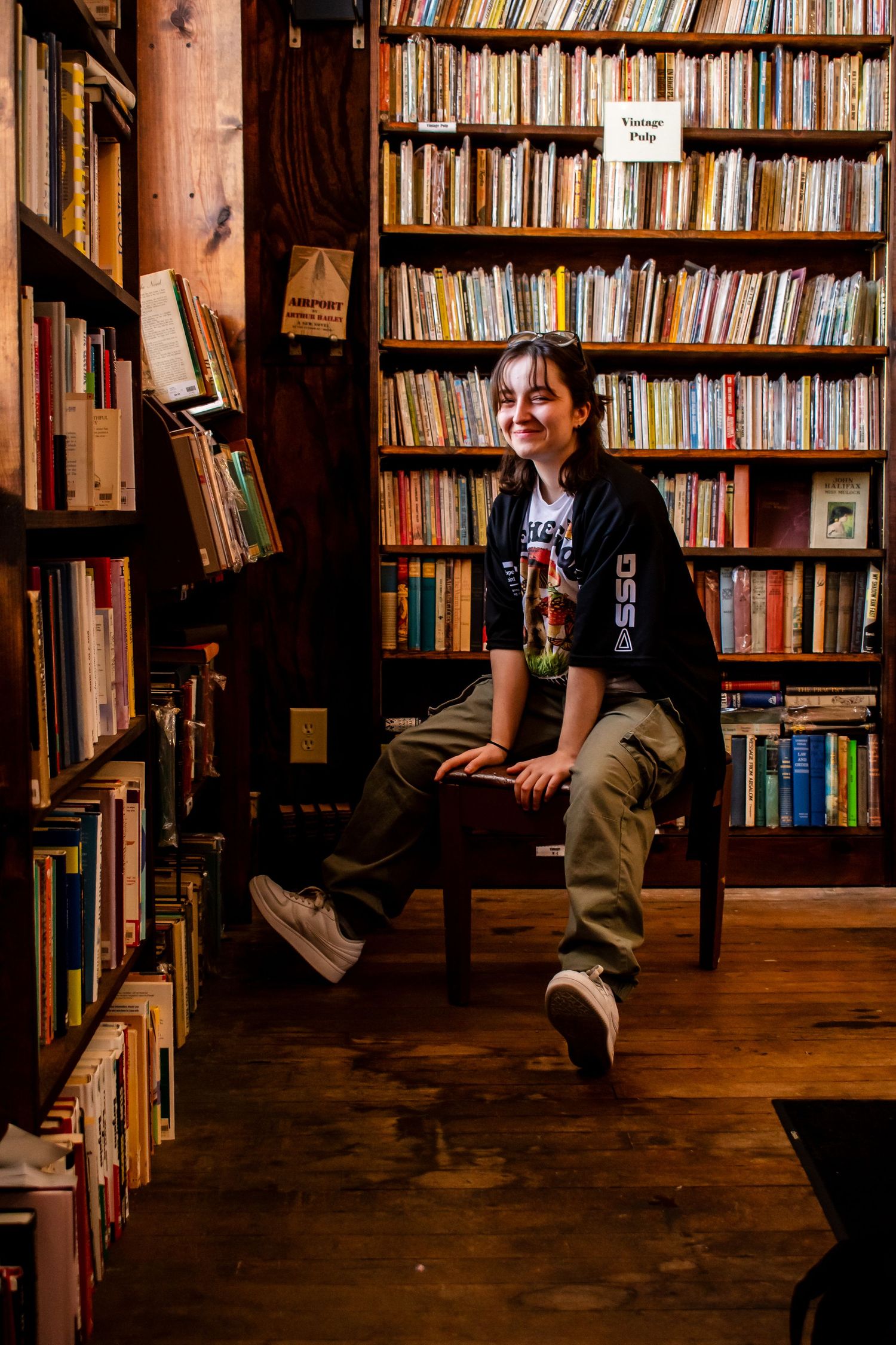Person sitting among rows of bookshelves in cozy library setting.
