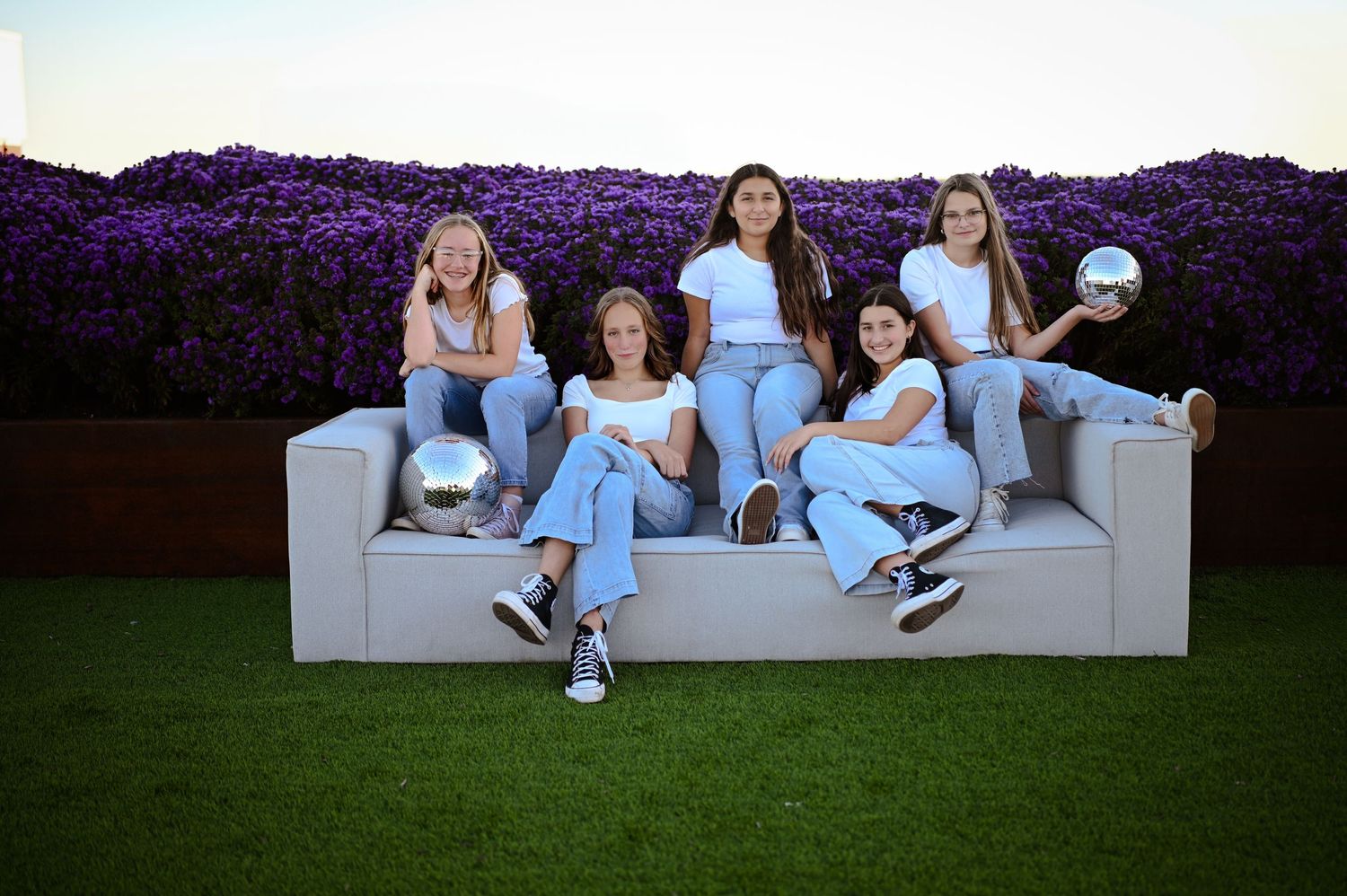 Group of friends in matching denim outfits lounging on a white couch against a purple backdrop.