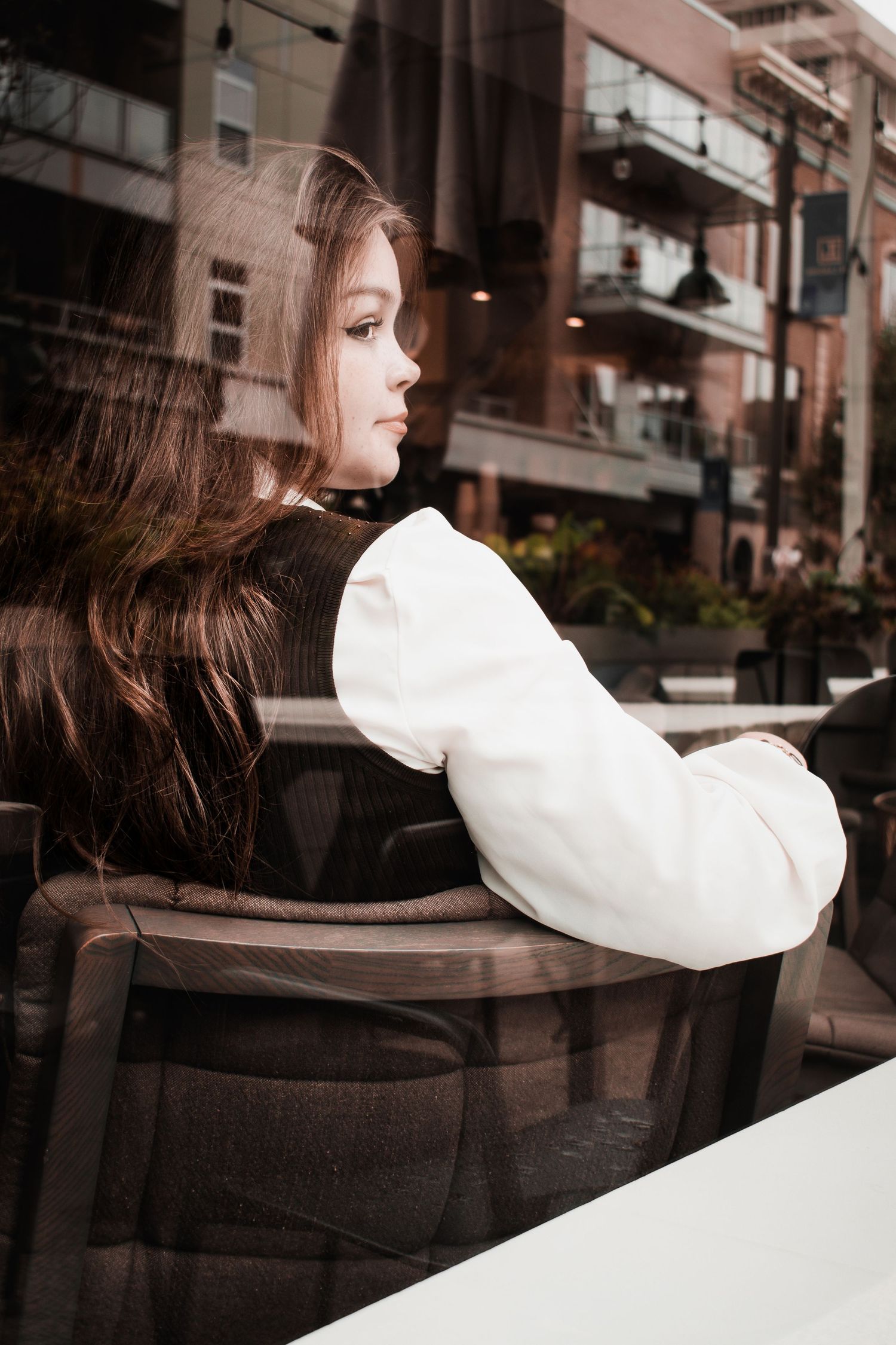 A artistic portrait through window glass showing a white poofy sleeve against urban architecture.