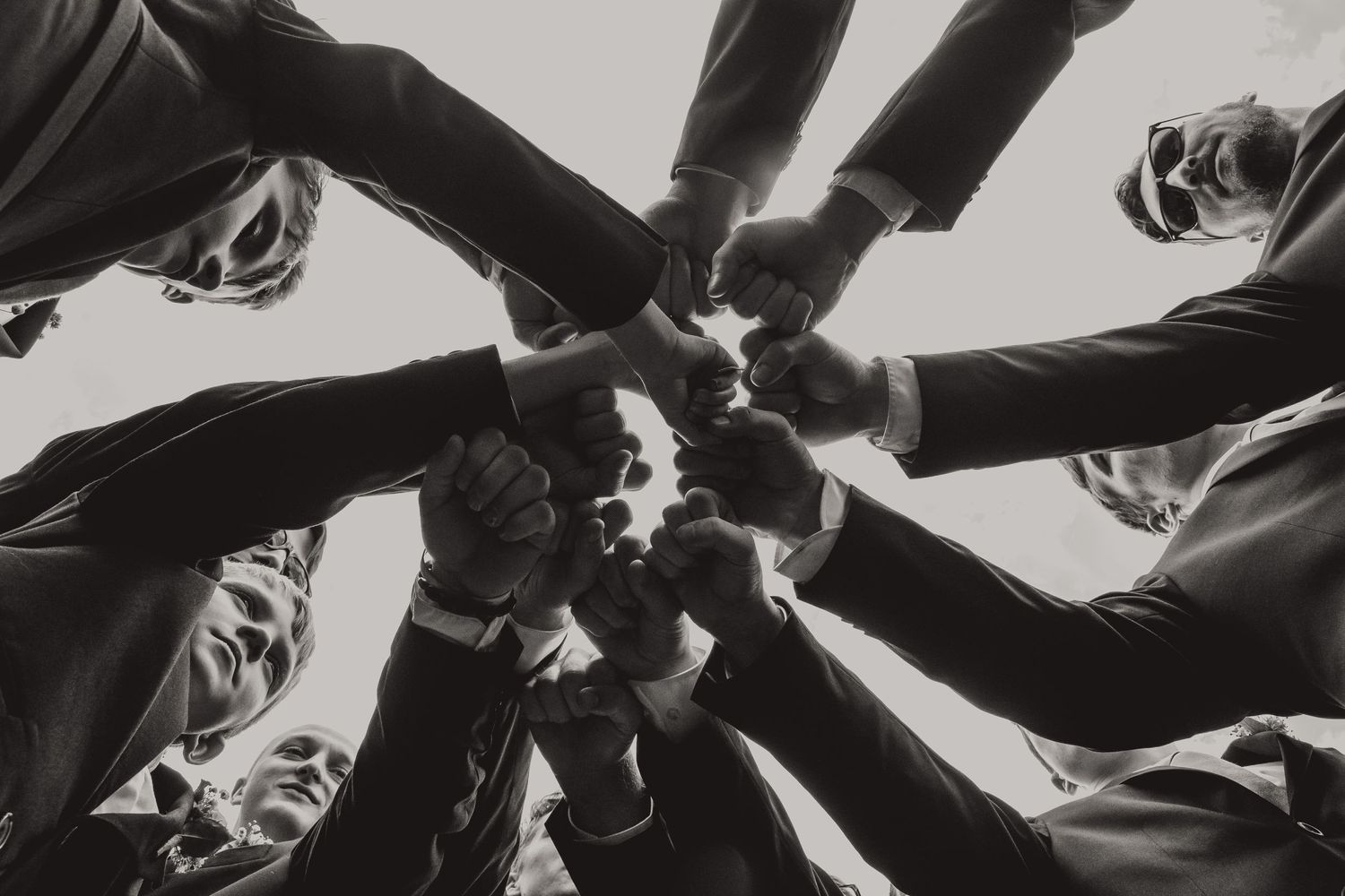 Black and white photo of hands joining together in unity circle from below.