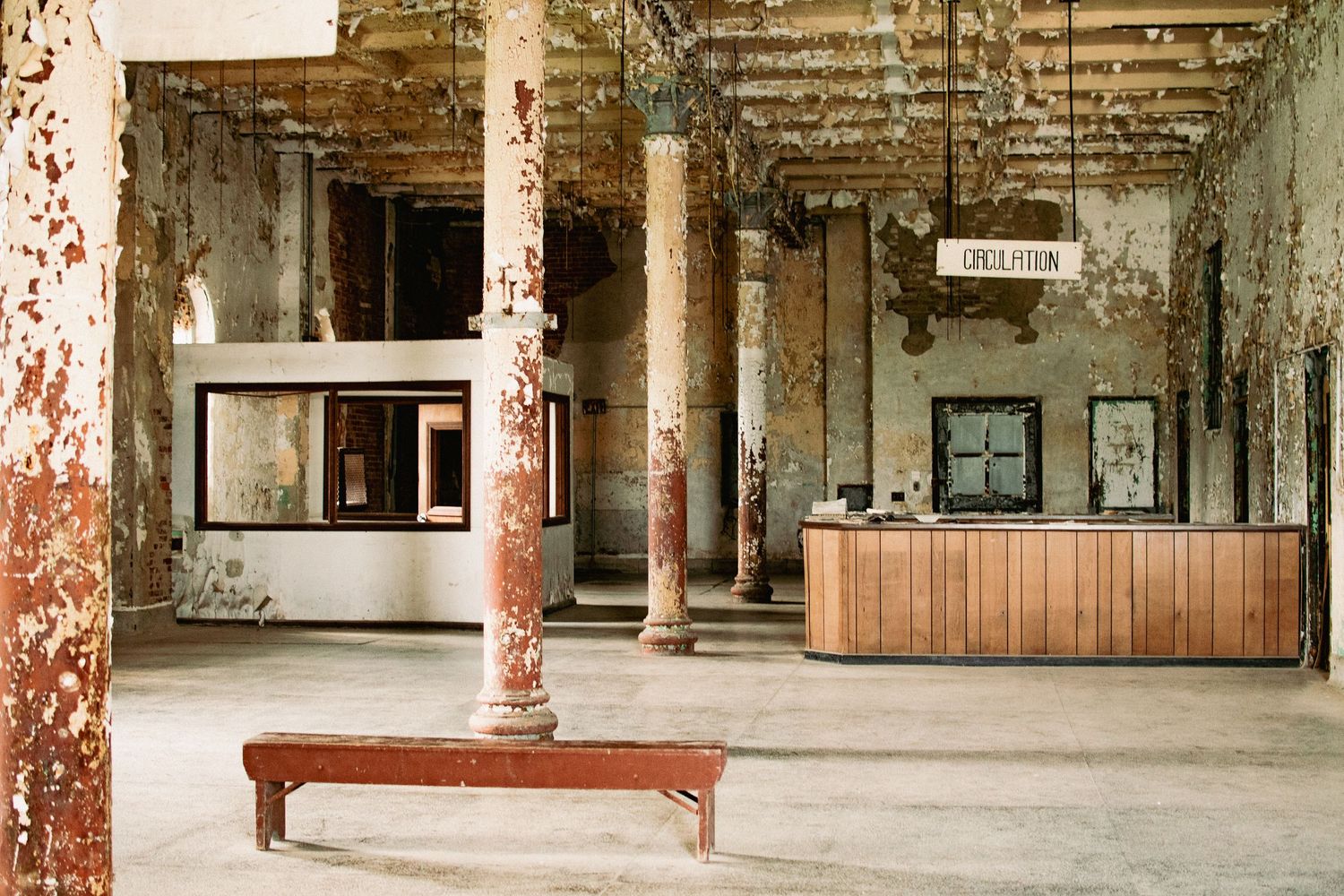 Abandoned lobby interior with peeling paint, weathered columns, and wooden reception desk in a dilapidated building.