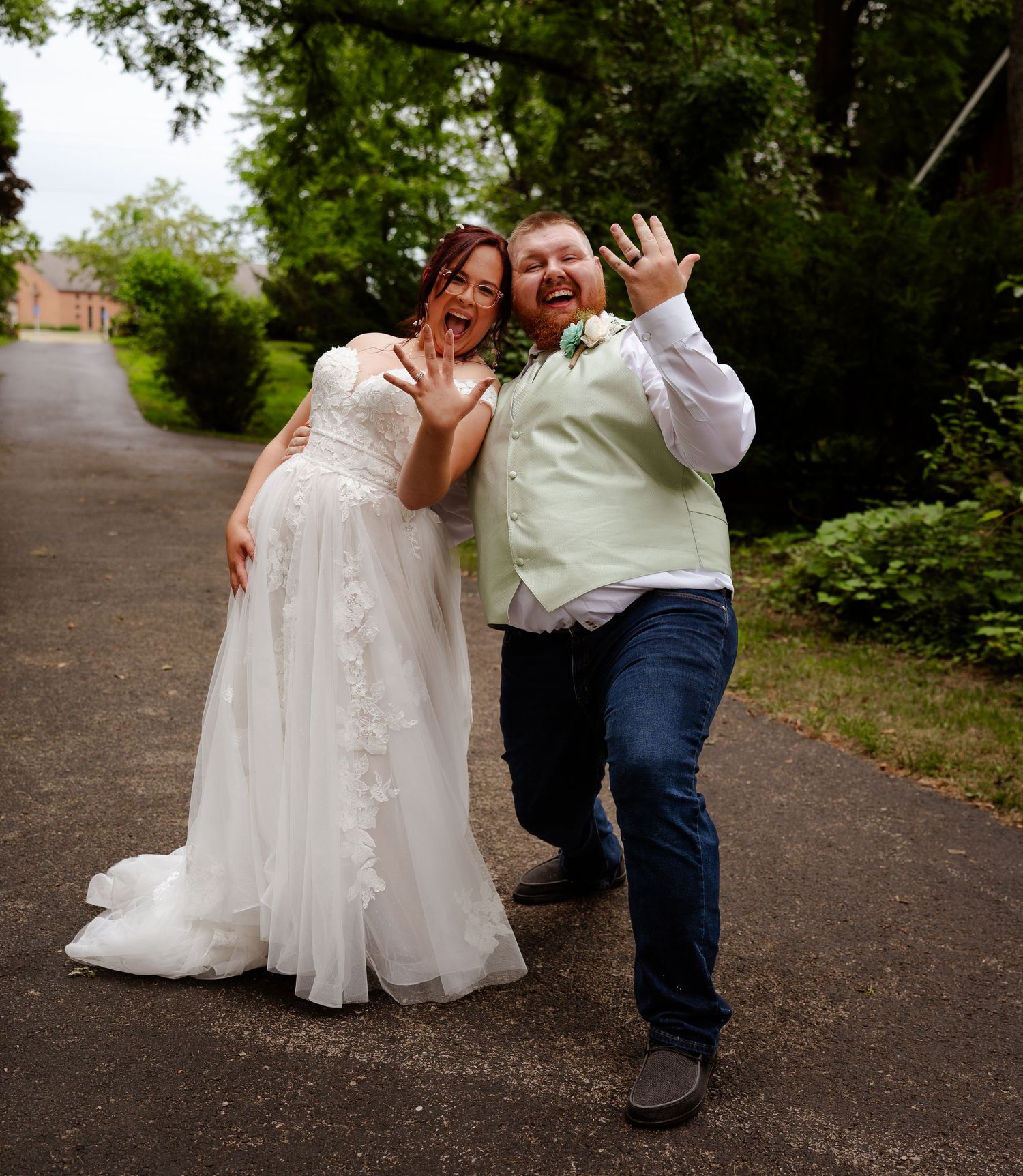 A couple shares joyful moments during an outdoor portrait session along a tree-lined path in casual attire.