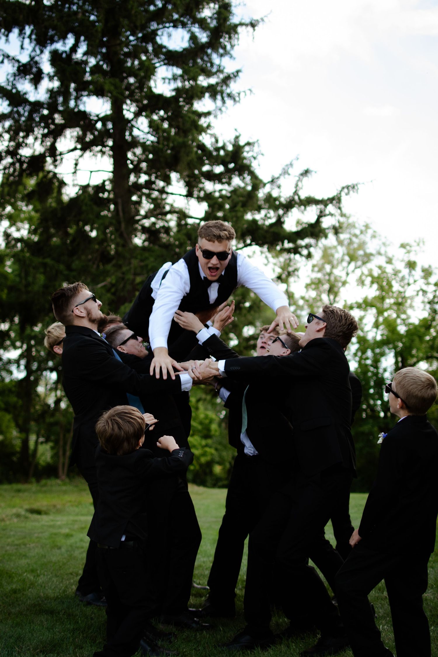 Groomsmen toss person in air during playful outdoor wedding photo.