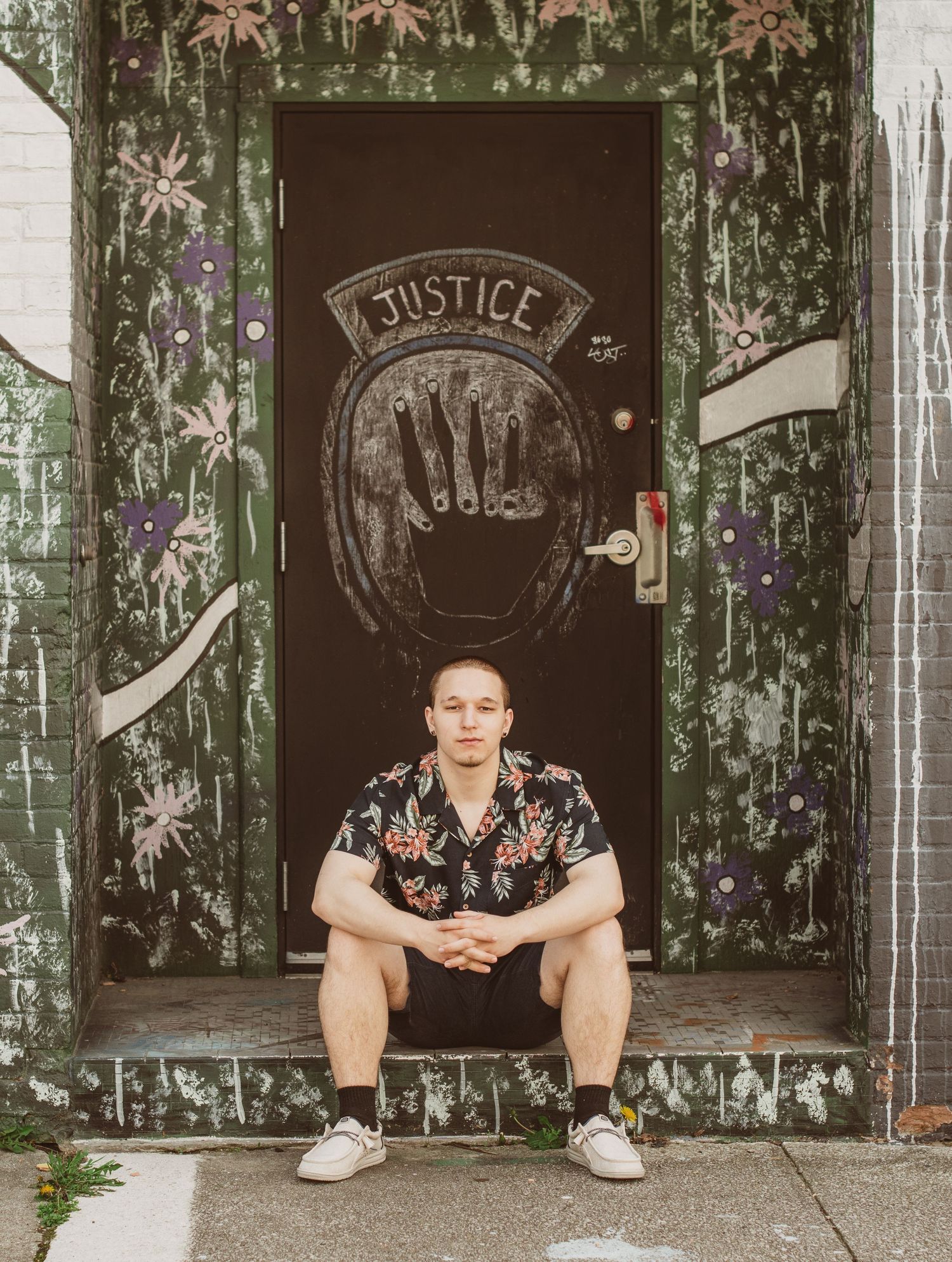 Figure seated on doorstep with artistic graffiti and floral decorations on door.
