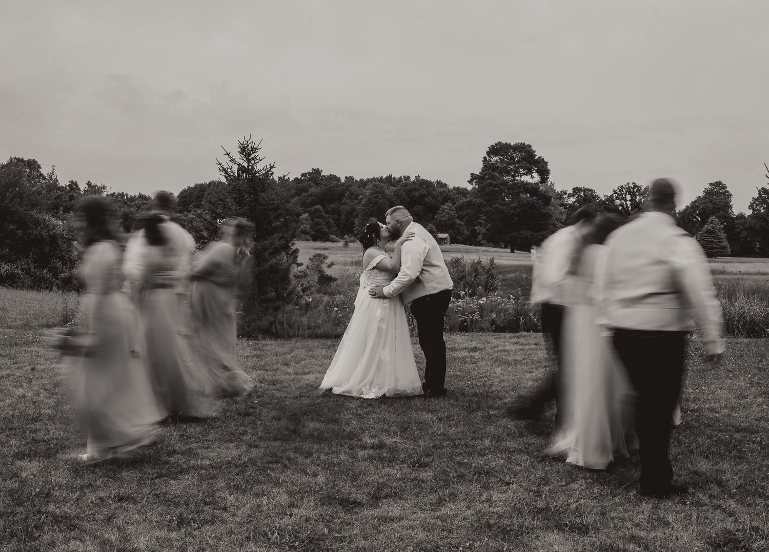 A vintage black and white photograph shows couples dancing in a field while two people embrace in the center.