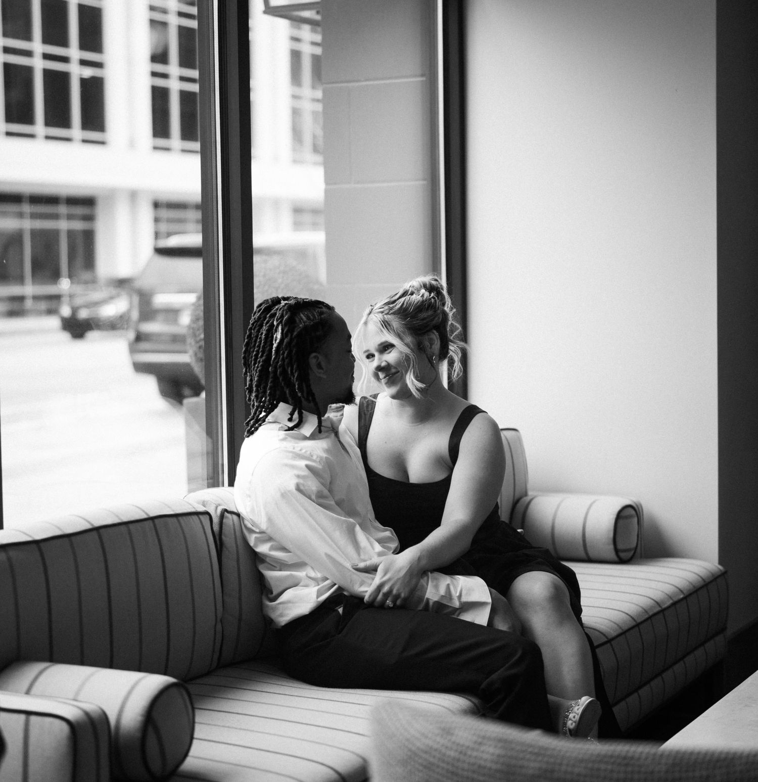 Intimate moment shared between two people sitting on a grey couch by a window.