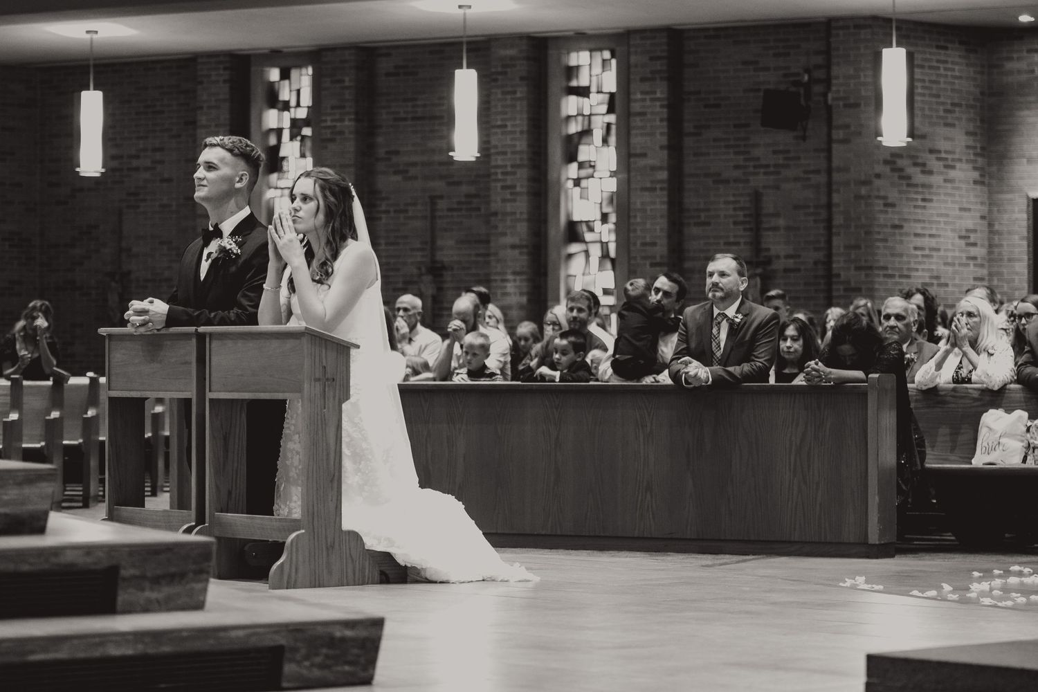 Black and white church wedding ceremony with guests seated in pews.