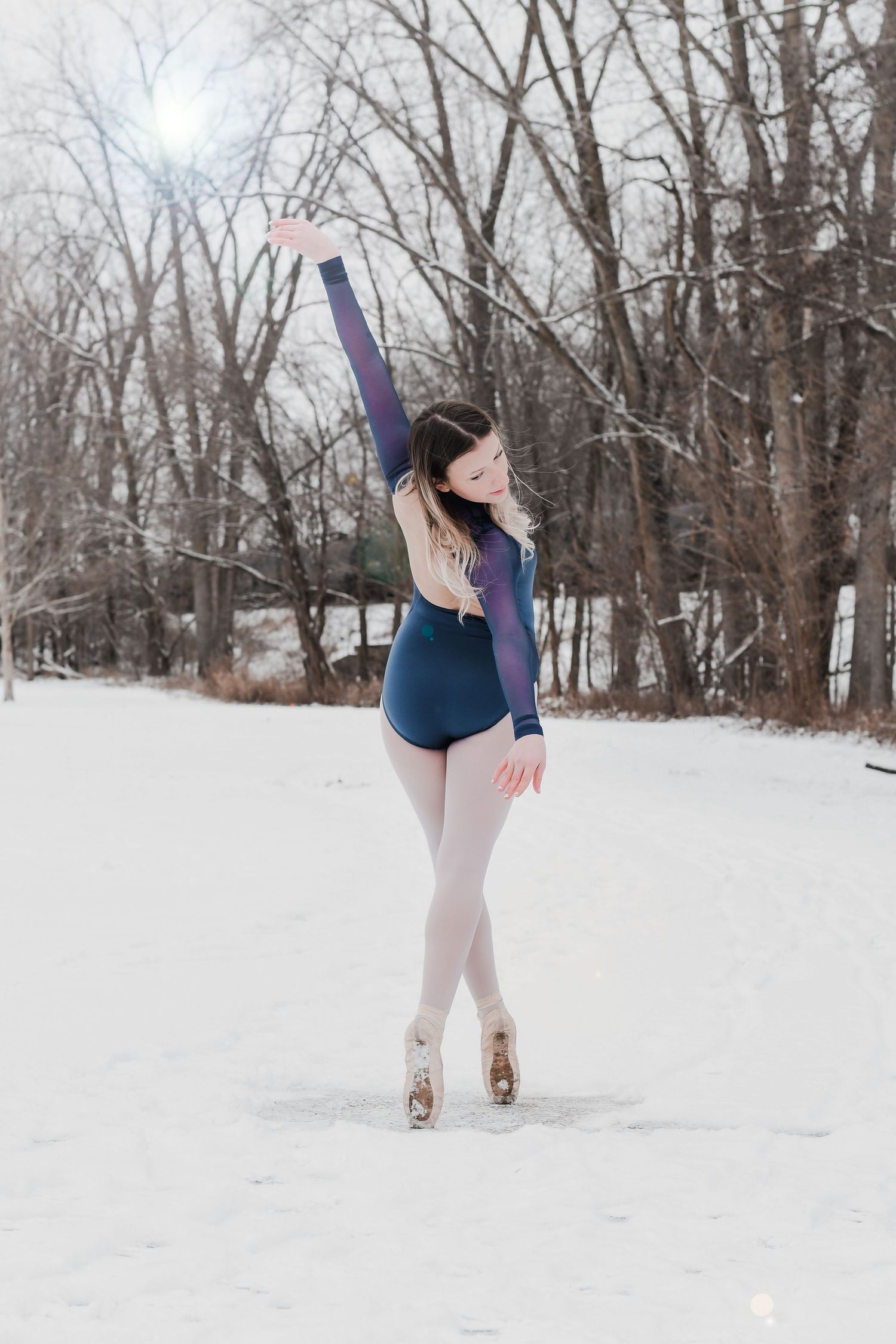 Ballet dancer poses gracefully in the snow wearing a blue leotard with white tights.