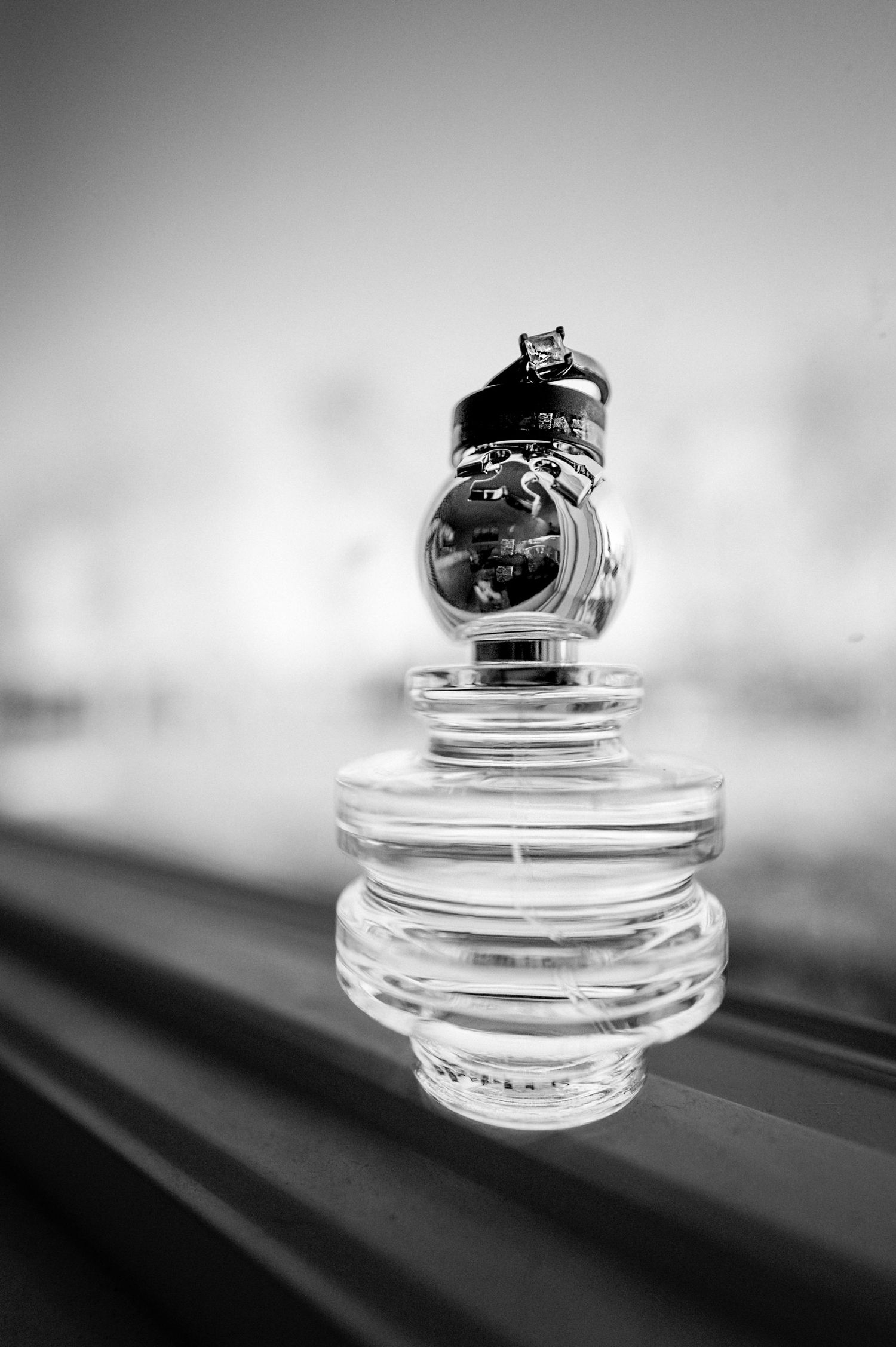 Close up black and white artistic shot of engagement ring balanced on glass bottle tops.